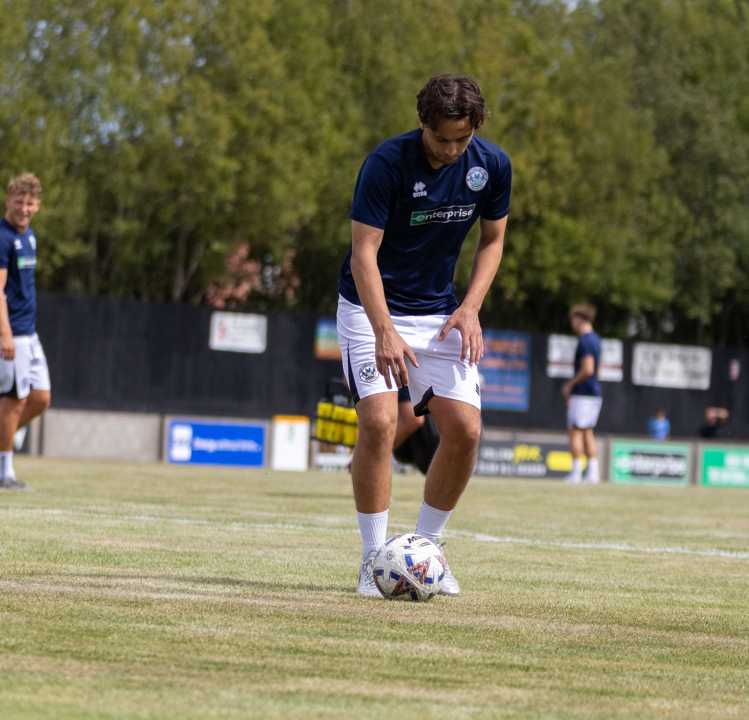 A soccer player in a navy blue kit controls a football on a grass pitch during an outdoor training session.