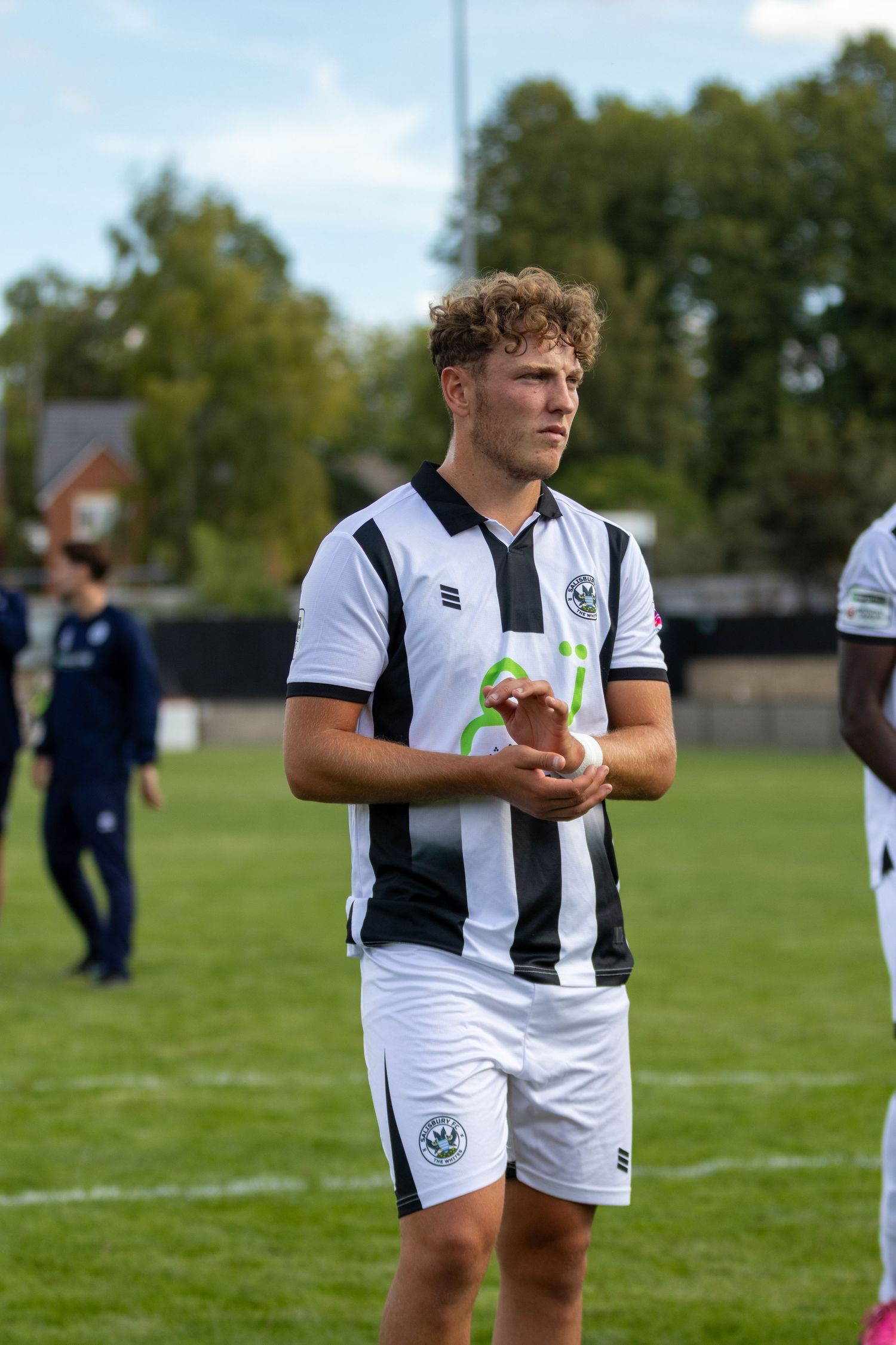 football player in black and white striped jersey holding a ball on a green field during a match.