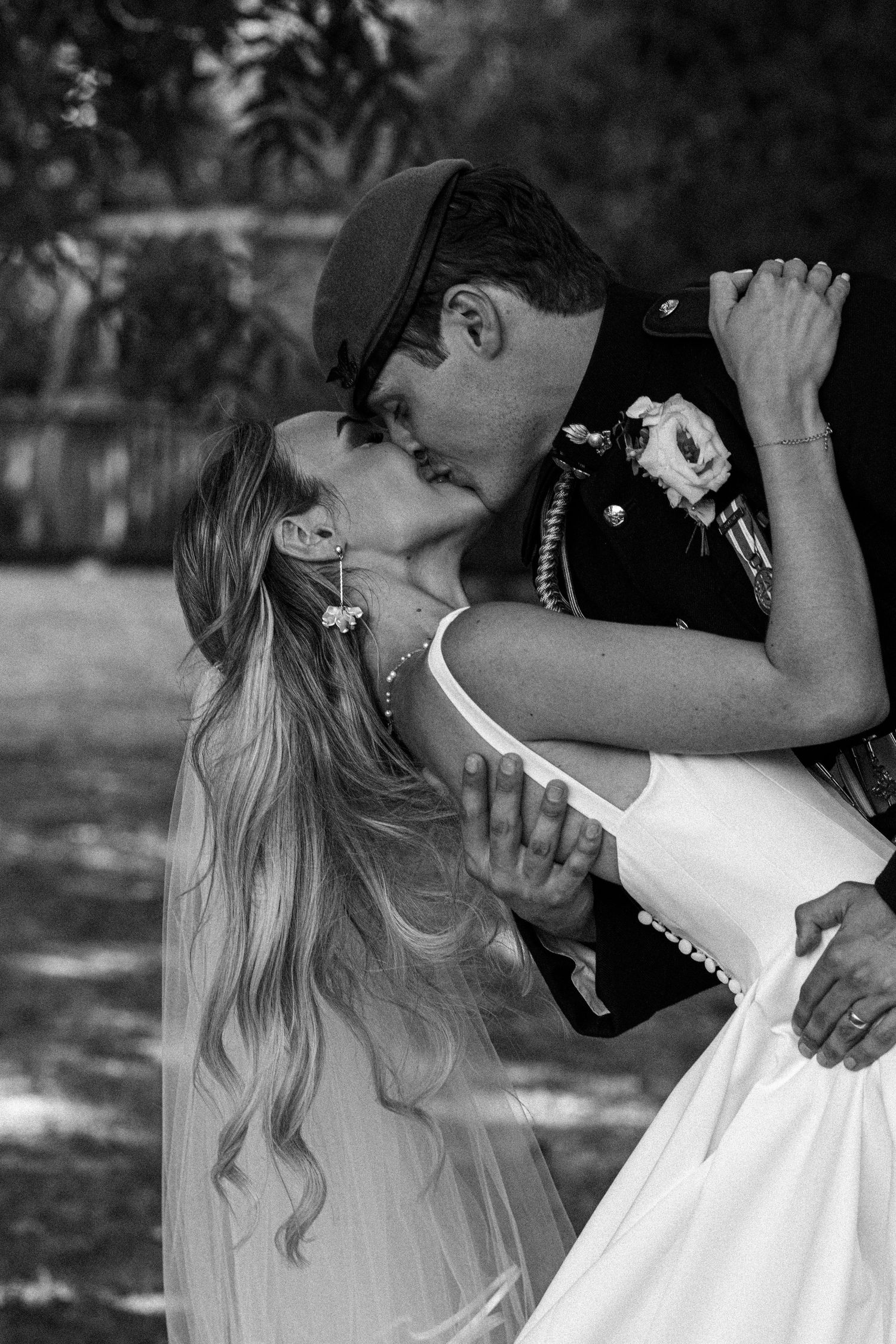 Black and white photo of a bride and groom sharing a romantic dip kiss outdoors on their wedding day.