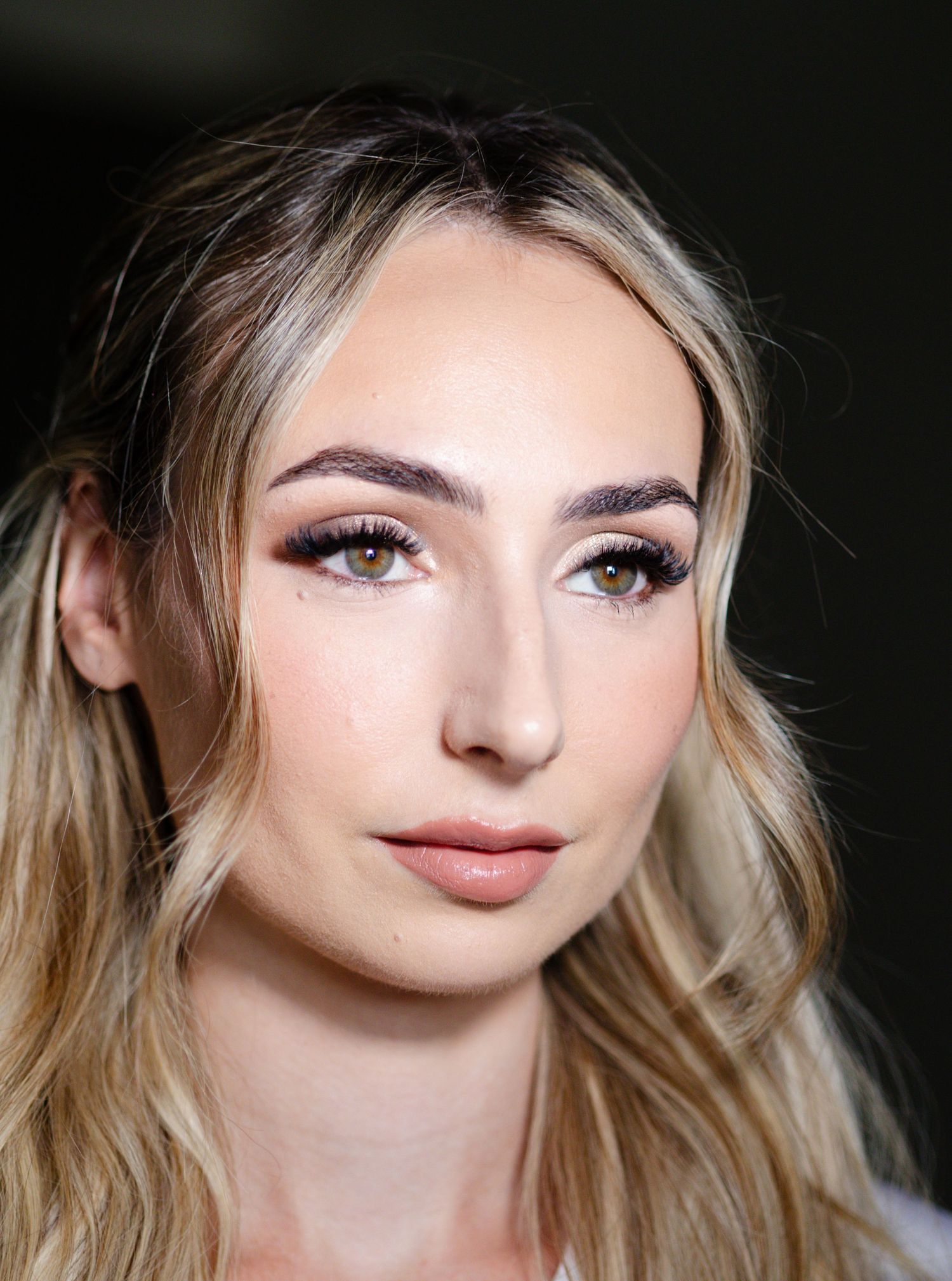 Young woman with blonde hair and natural makeup featuring defined brows and subtle eye makeup poses for portrait.
