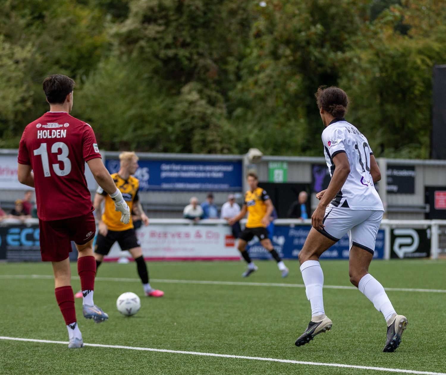 Soccer players compete on a green field, with player number 13 Holden in red uniform dribbling the ball.