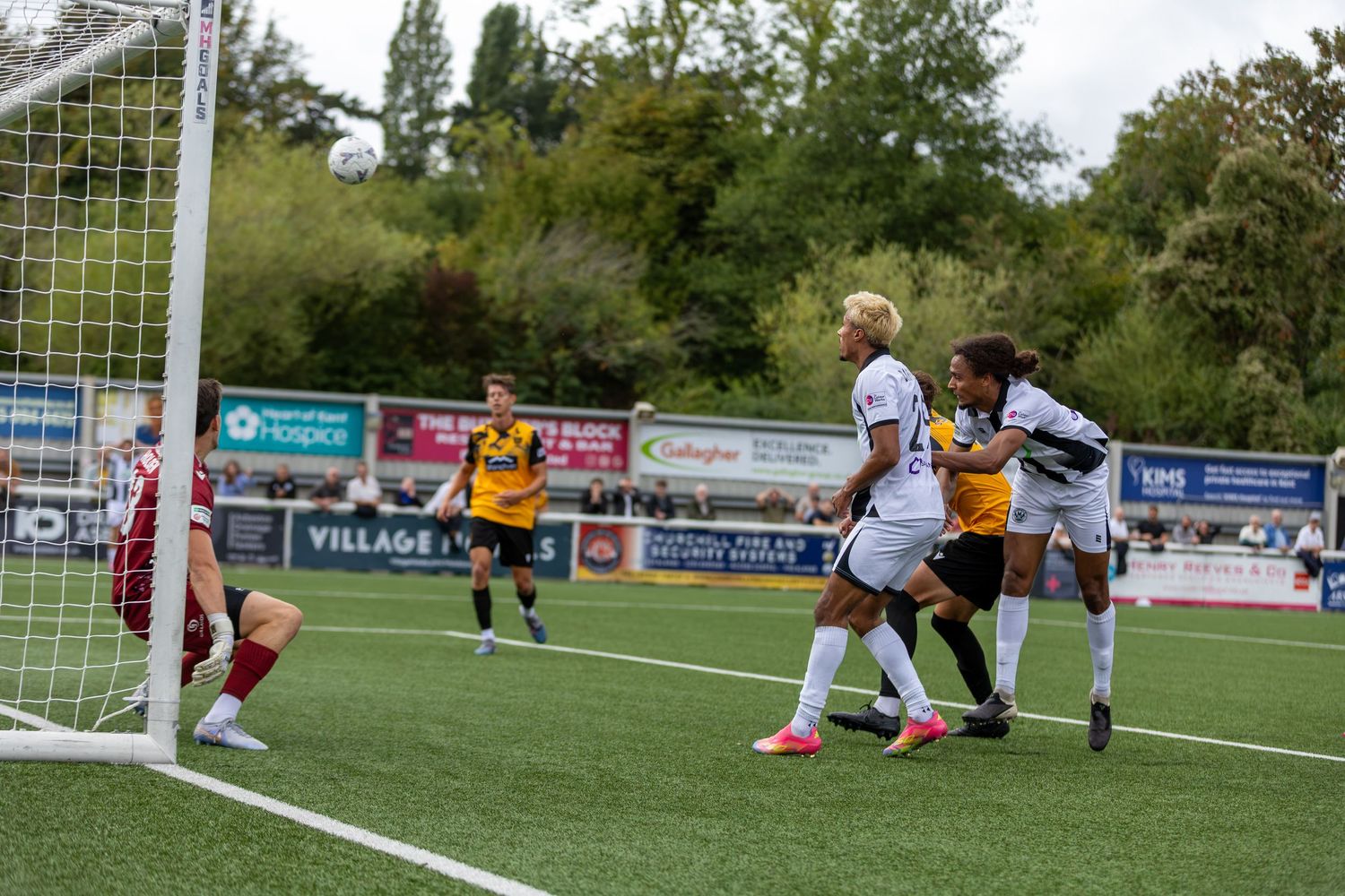 Soccer players compete for the ball near the goal during an outdoor match on a green pitch.