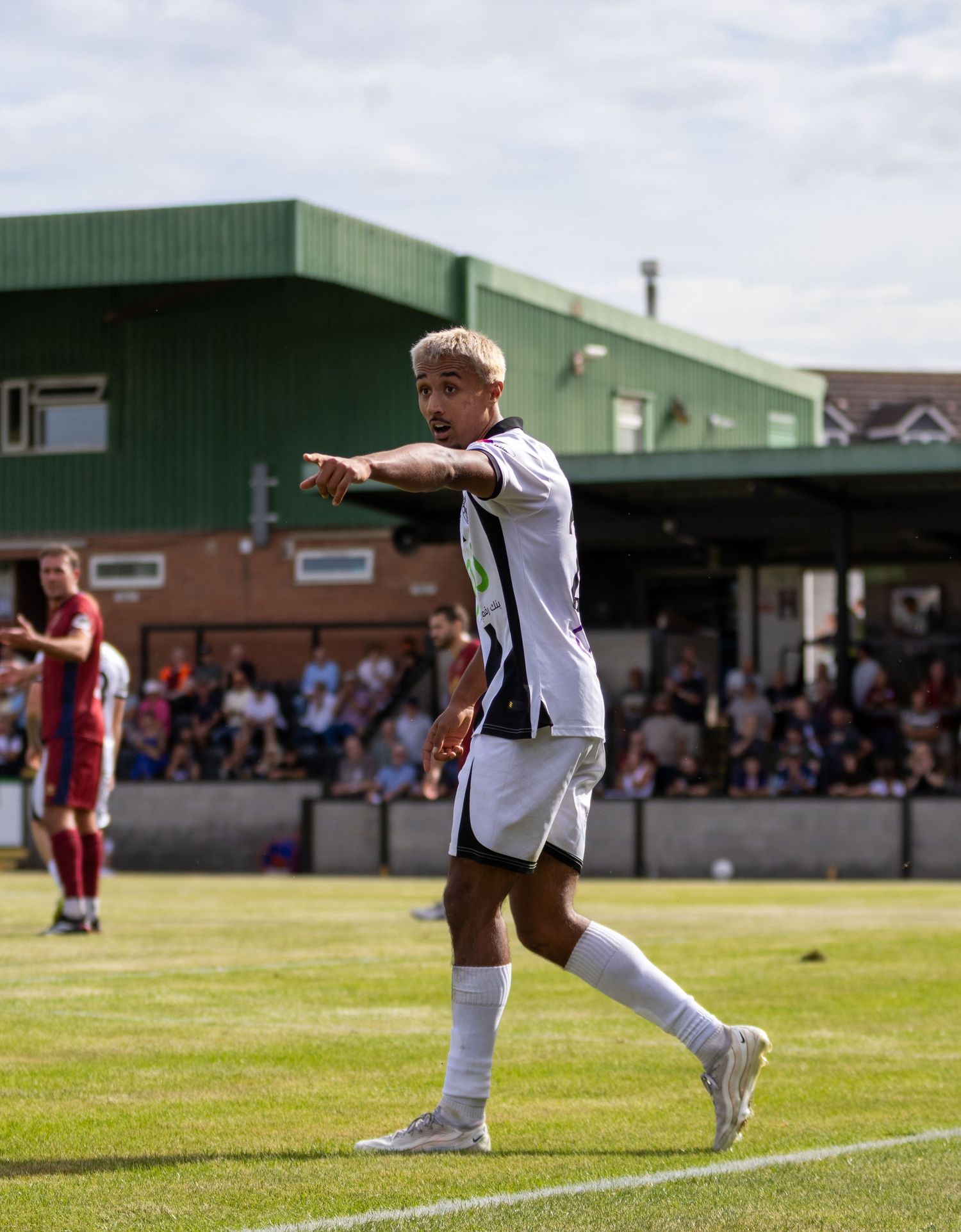 A blond soccer player in a black and white kit gestures with a pointed finger during a match.