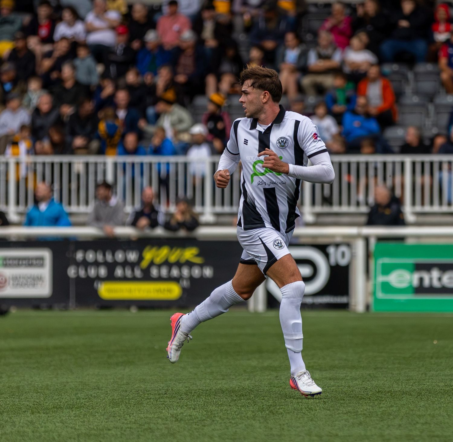 Soccer player in white and black uniform running on field during a match with fans in the background.