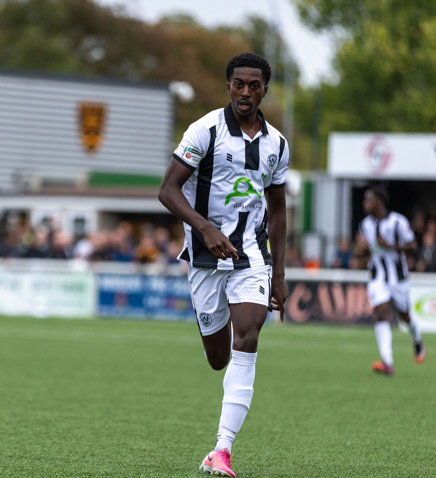 Soccer player in white and black kit running on green field during a match.