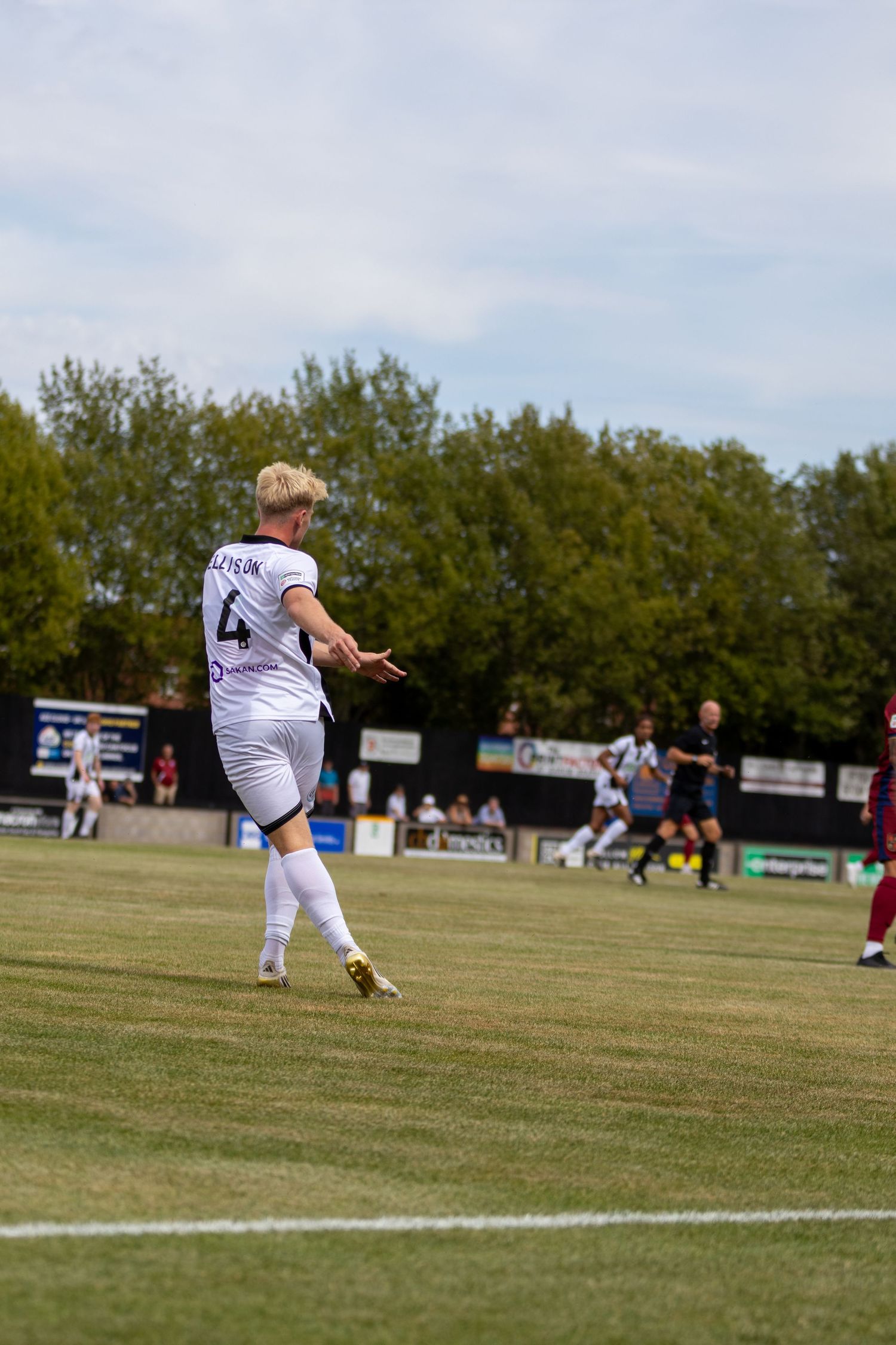 Number 4 footballer in white kit gestures while playing outdoor match on sunny afternoon.