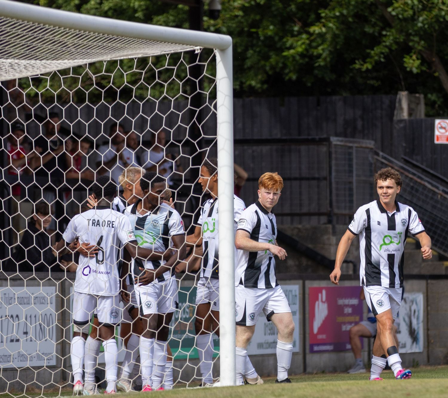 Salisbury FC players in black and white celebrate a goal together near the net during a home match.