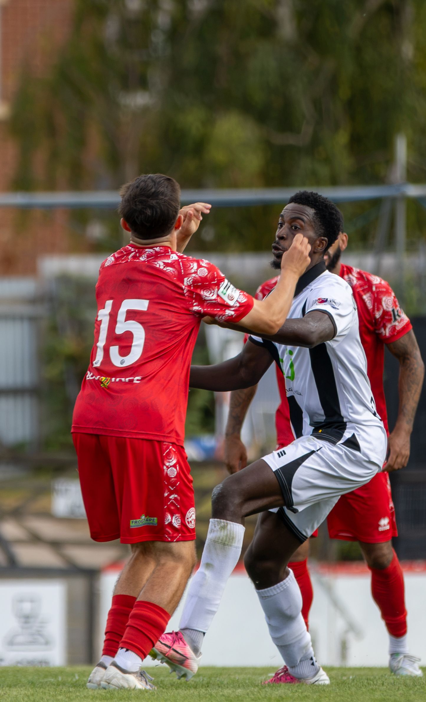 Two soccer players in red and white uniforms clash during a competitive match on a green field.