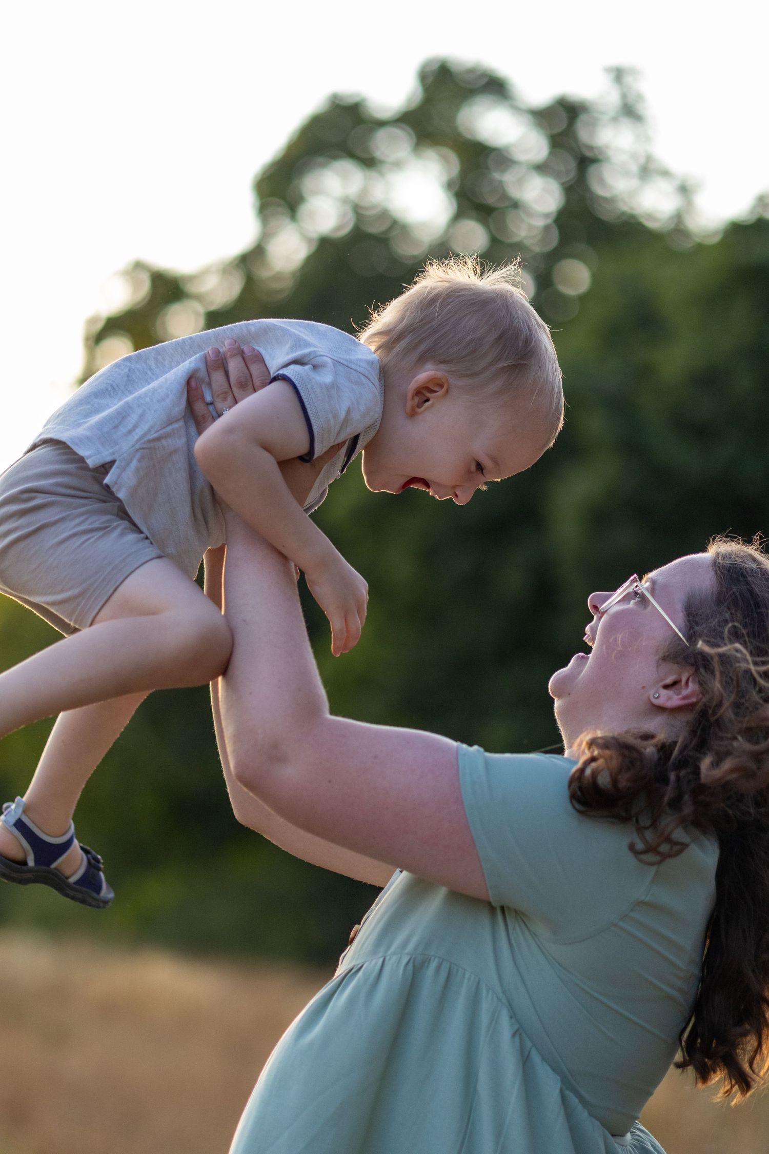 Mother lifting laughing toddler high in the air during outdoor family session at golden hour.