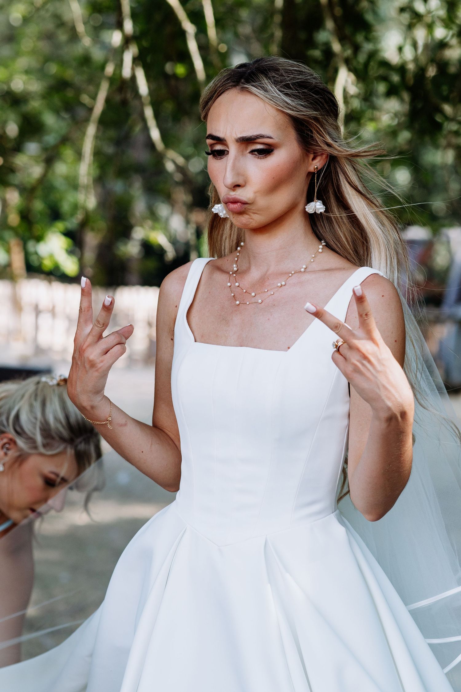 Beautiful blonde bride in elegant white square-neck wedding gown making a playful peace sign gesture.