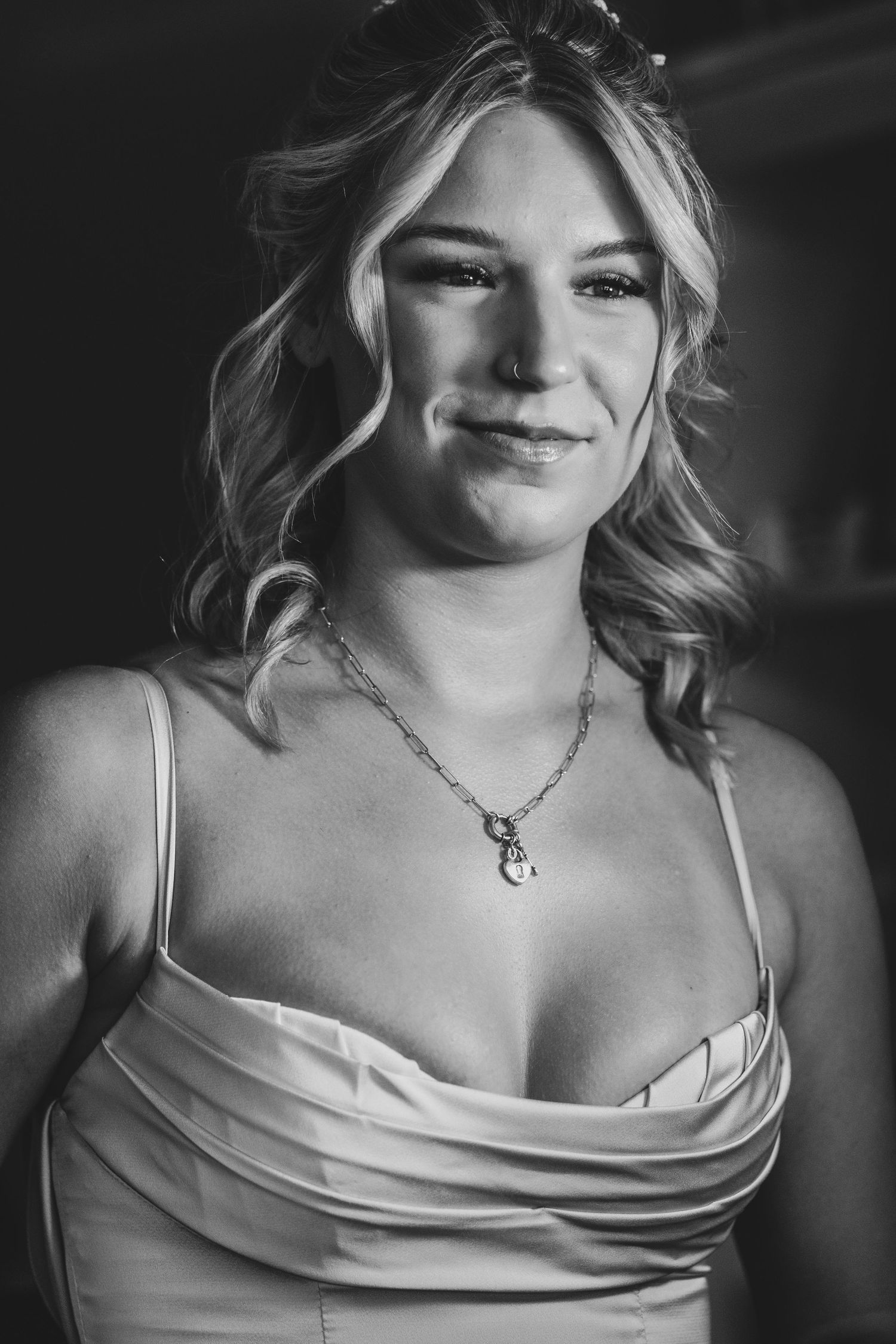 Black and white portrait of smiling blonde woman in formal dress with necklace at wedding event.