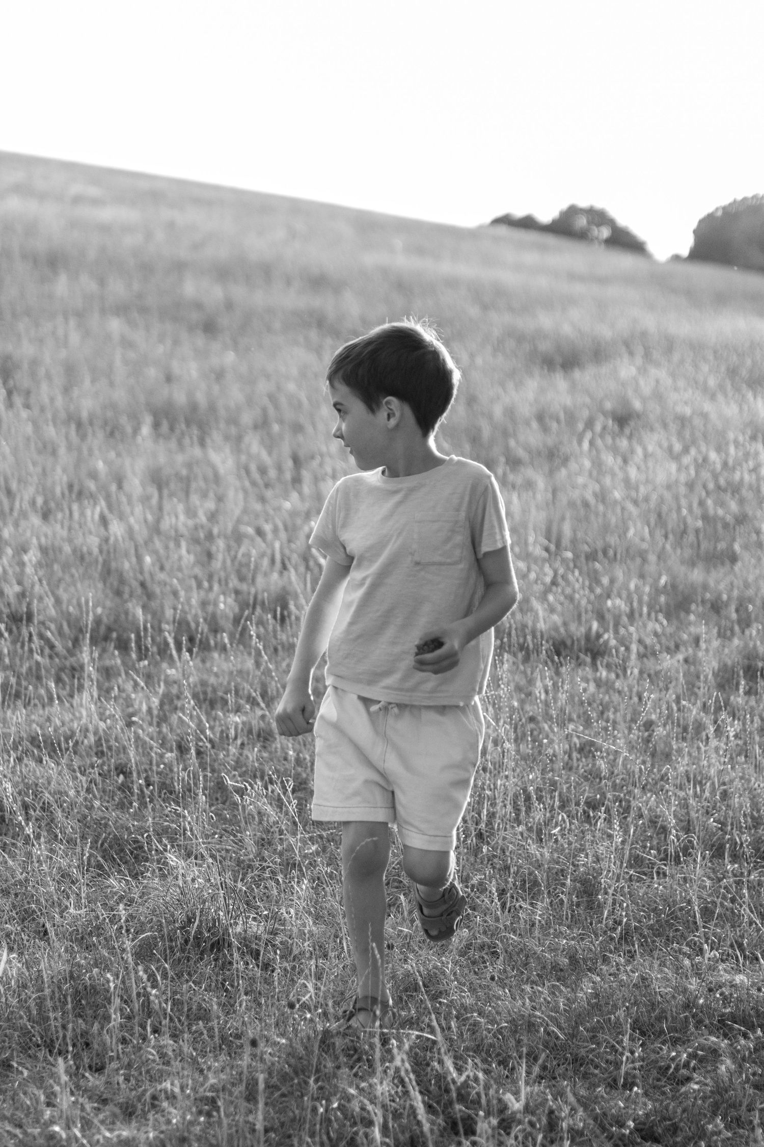 Black and white photo of a young boy running through a grassy field in summer.