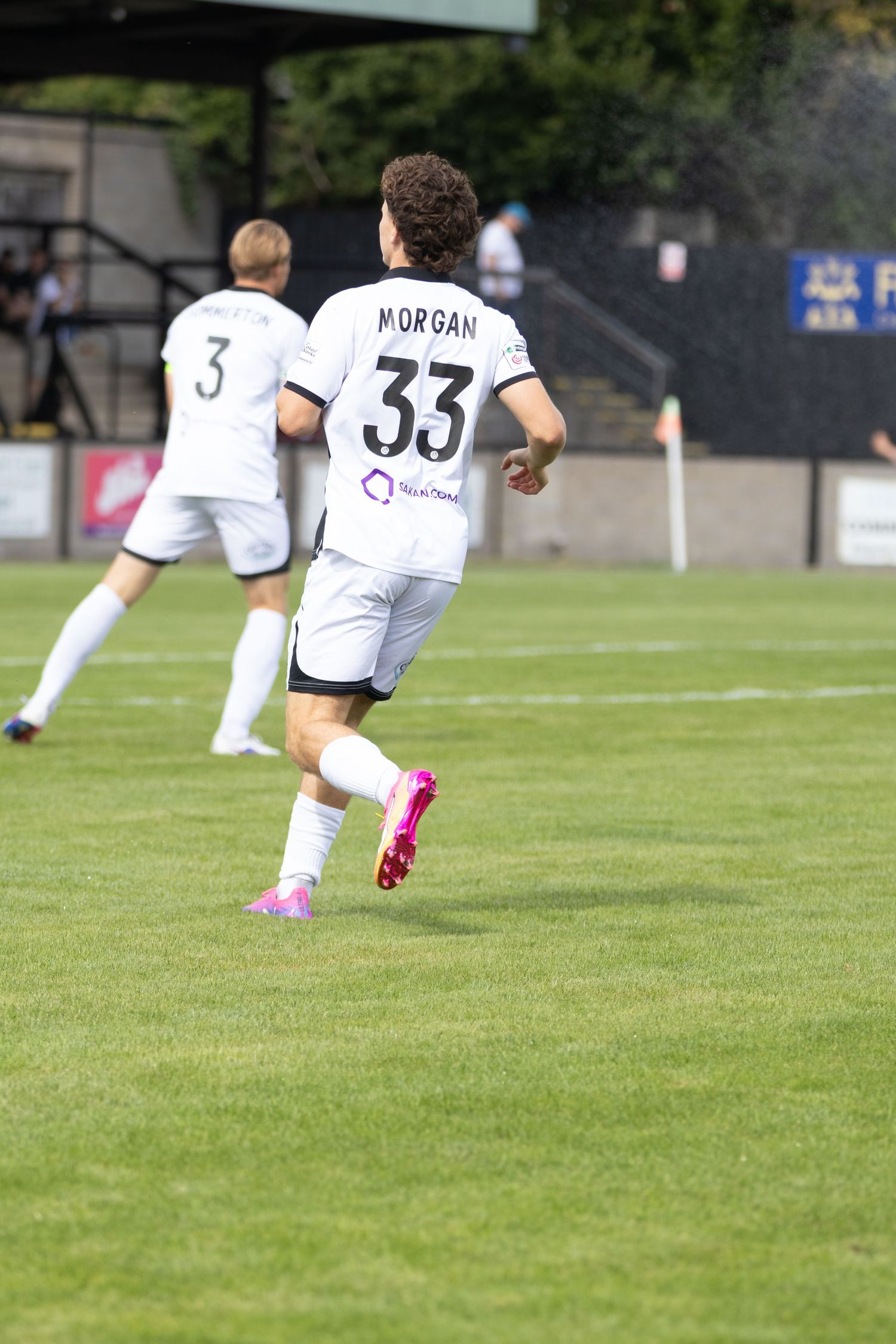 Football player Morgan number 33 in white kit runs across green pitch with teammate number 3 behind.
