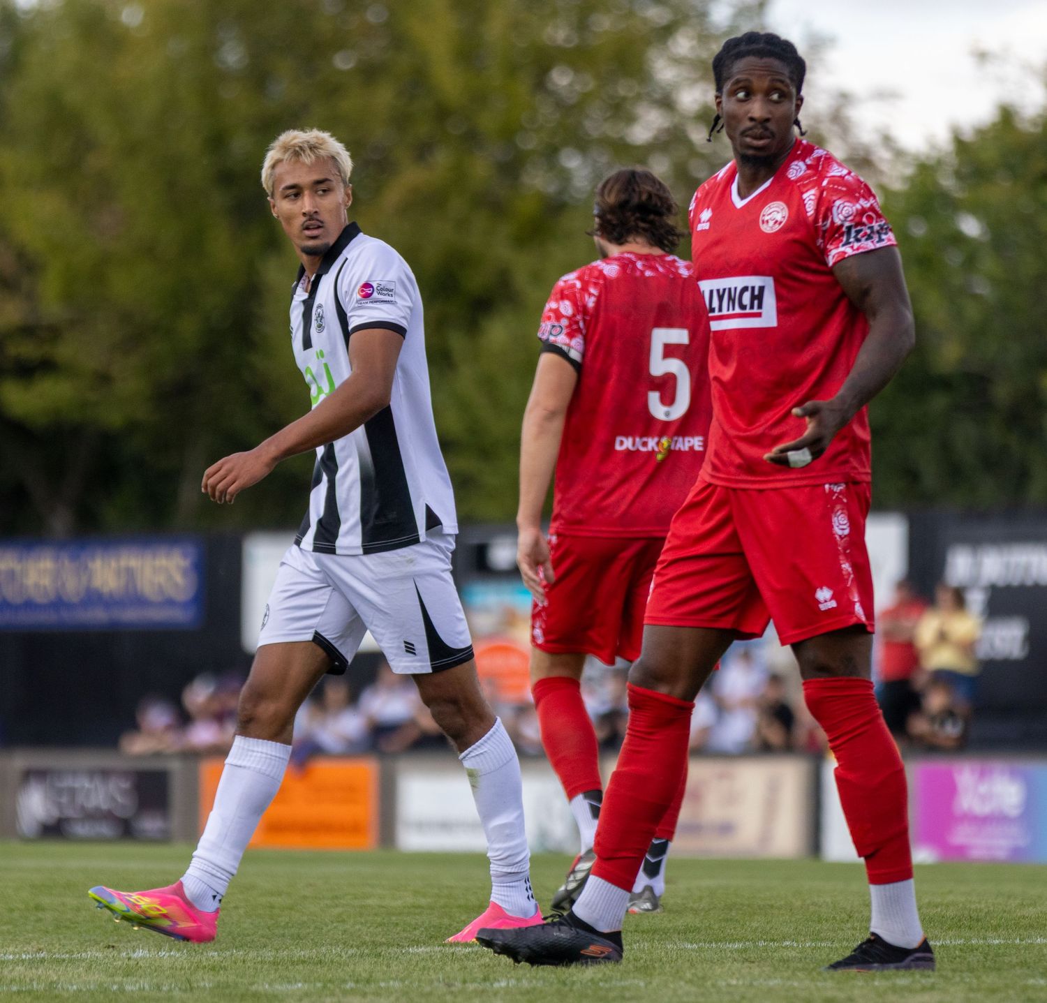 A black-and-white kitted player and red-kitted number 5 face off during a non-league football match.
