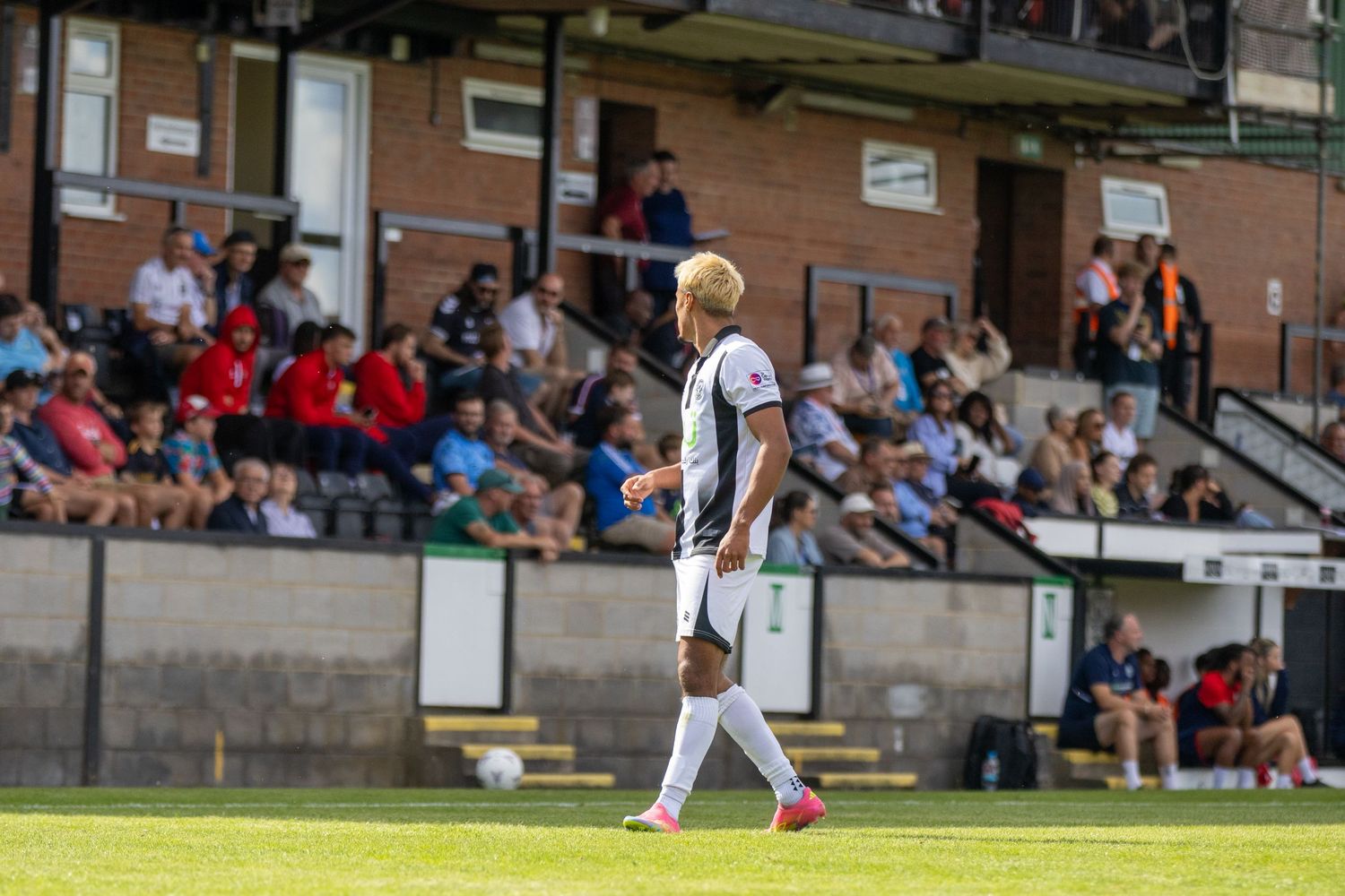 Soccer player in white kit walks along the sideline in front of a packed stadium.
