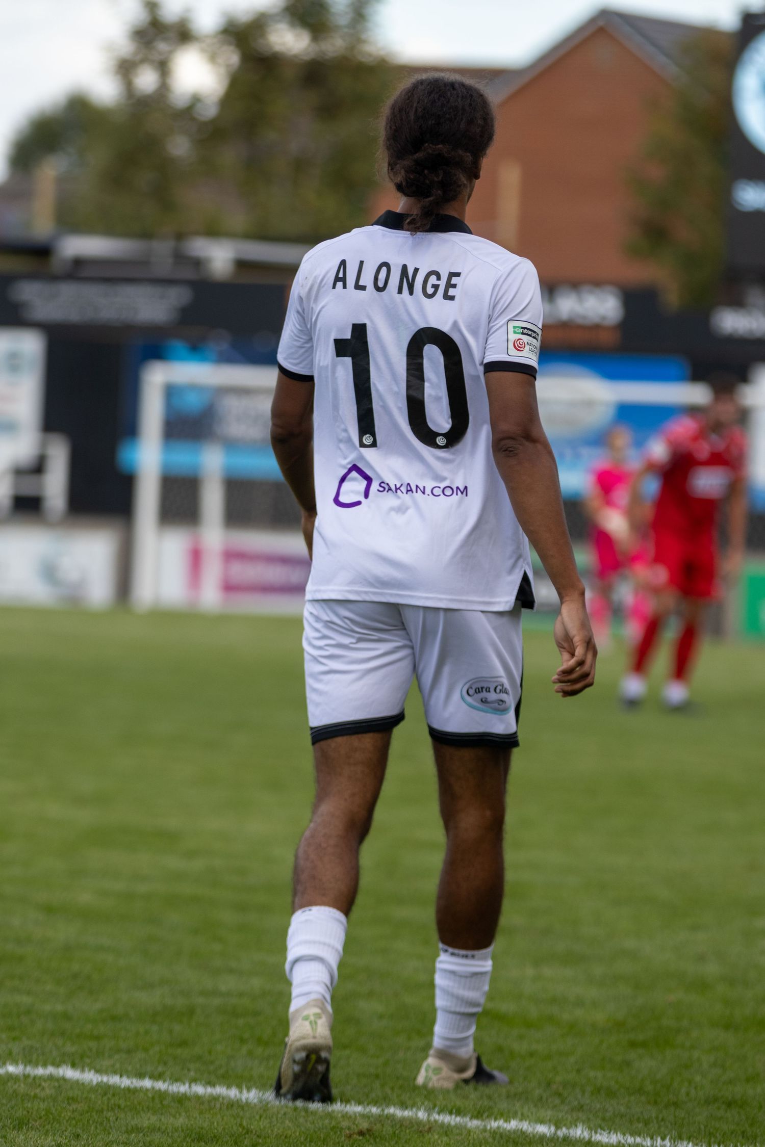Soccer player Alonge wearing number 10 white jersey walks on green pitch during a football match.
