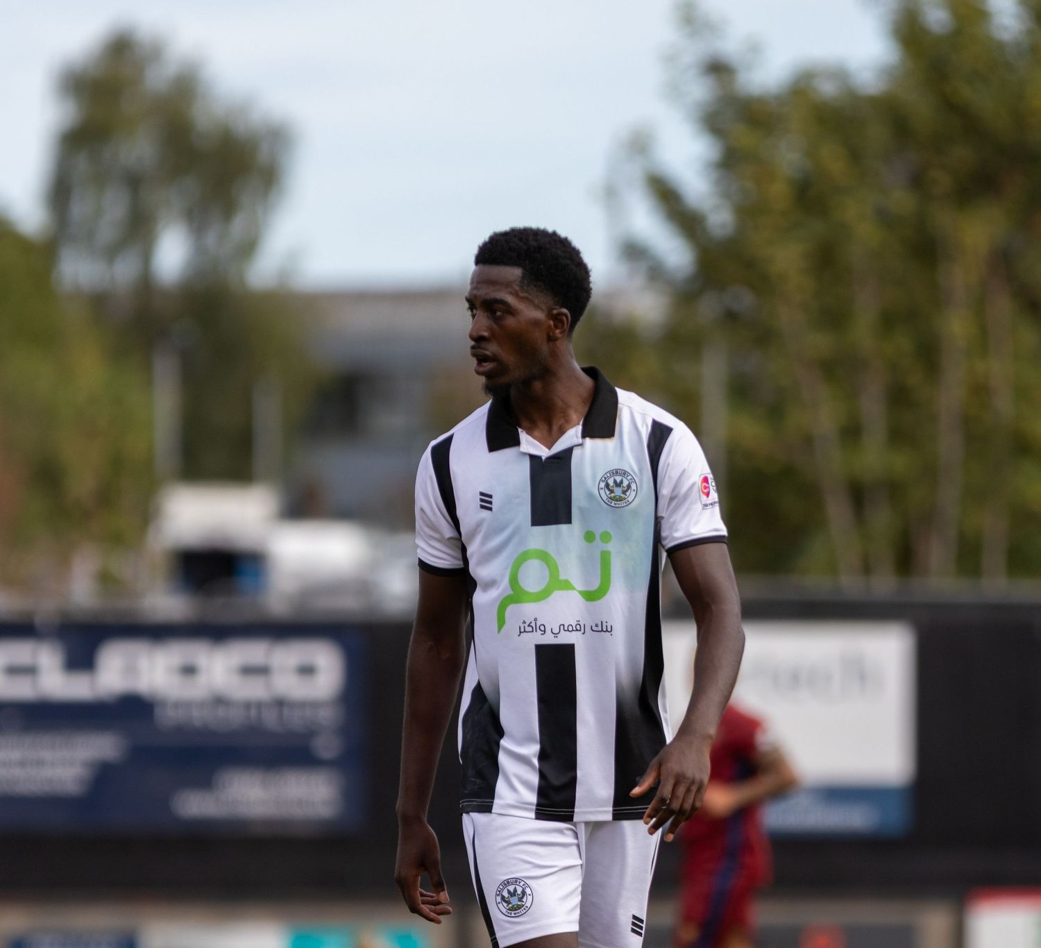 Black and white kit football player looks focused during an outdoor match on a sunny day.