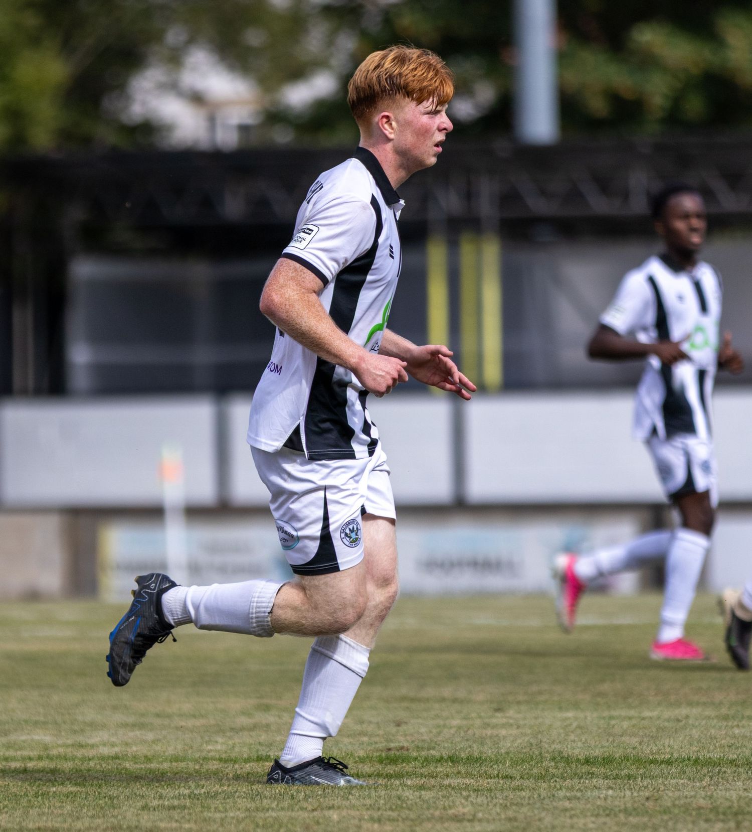 Young red-haired soccer player in black and white strip runs on grass during a football match.