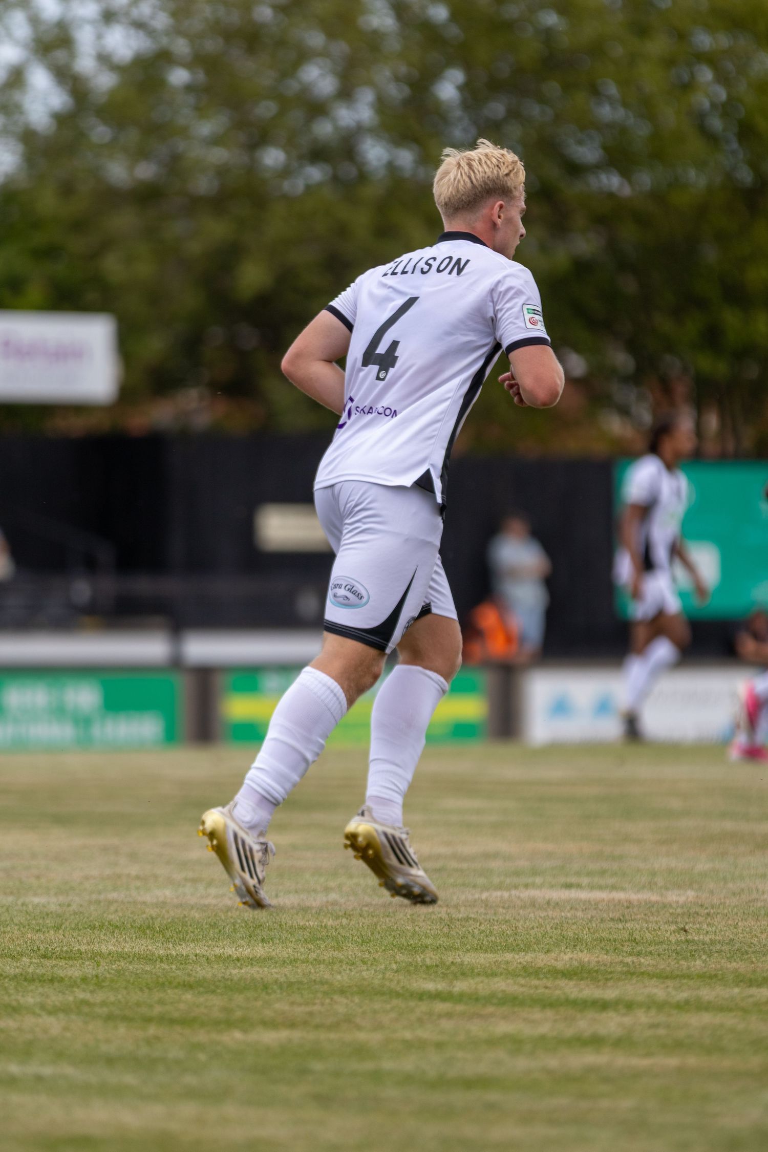 A blonde footballer wearing number 4 Ellison jersey in white kit runs on a pitch.