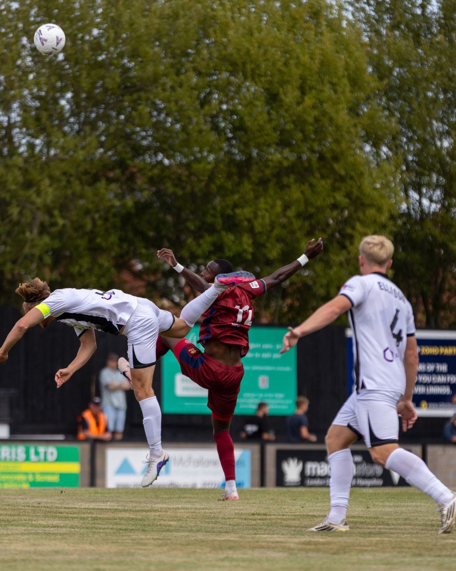 A soccer player performs an acrobatic bicycle kick during a match while opponents in white jerseys look on.