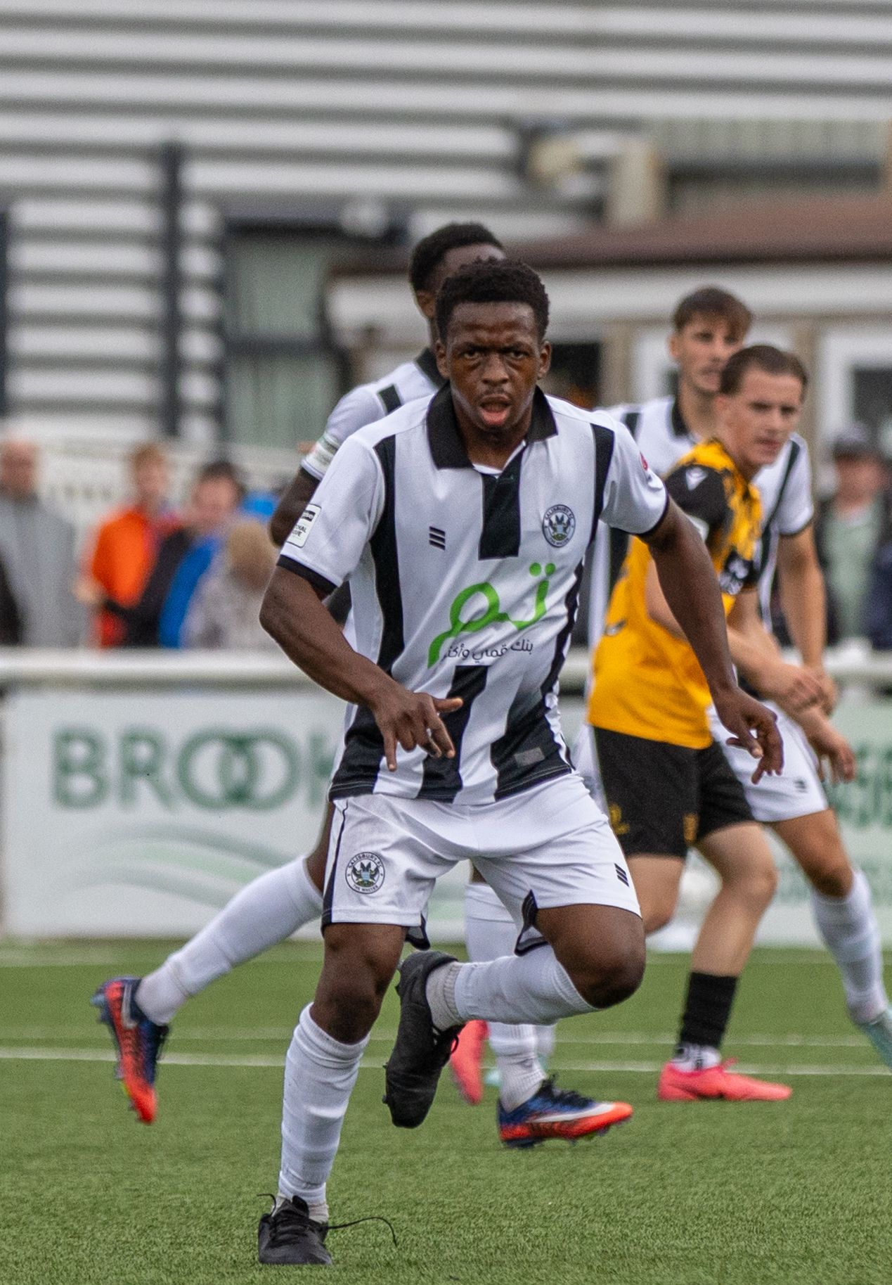 A young soccer player in black and white kit sprints during a match on a green field.