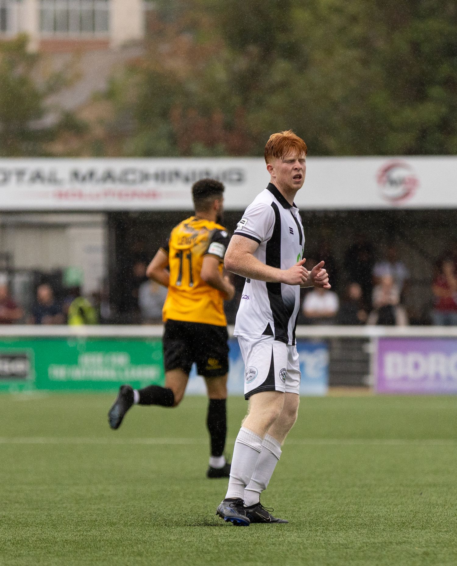 Red-haired soccer player in black and white kit stands on green pitch during a competitive football match.