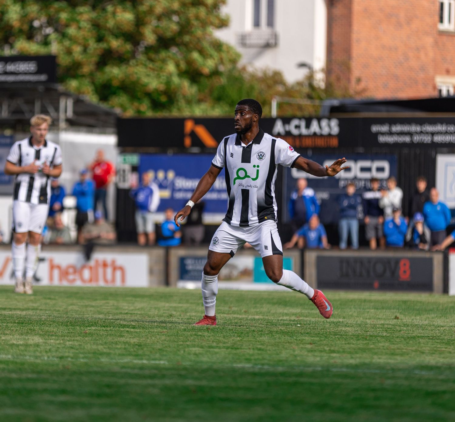 A soccer player in black and white kit dribbles on a green pitch during a sunny outdoor match.