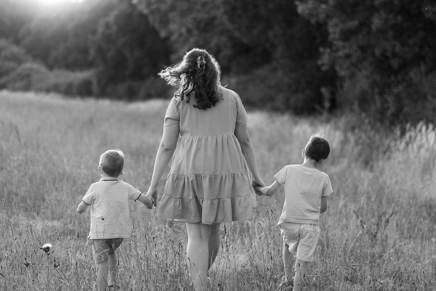 Black and white photo of a mother walking hand in hand with two young children in a meadow.