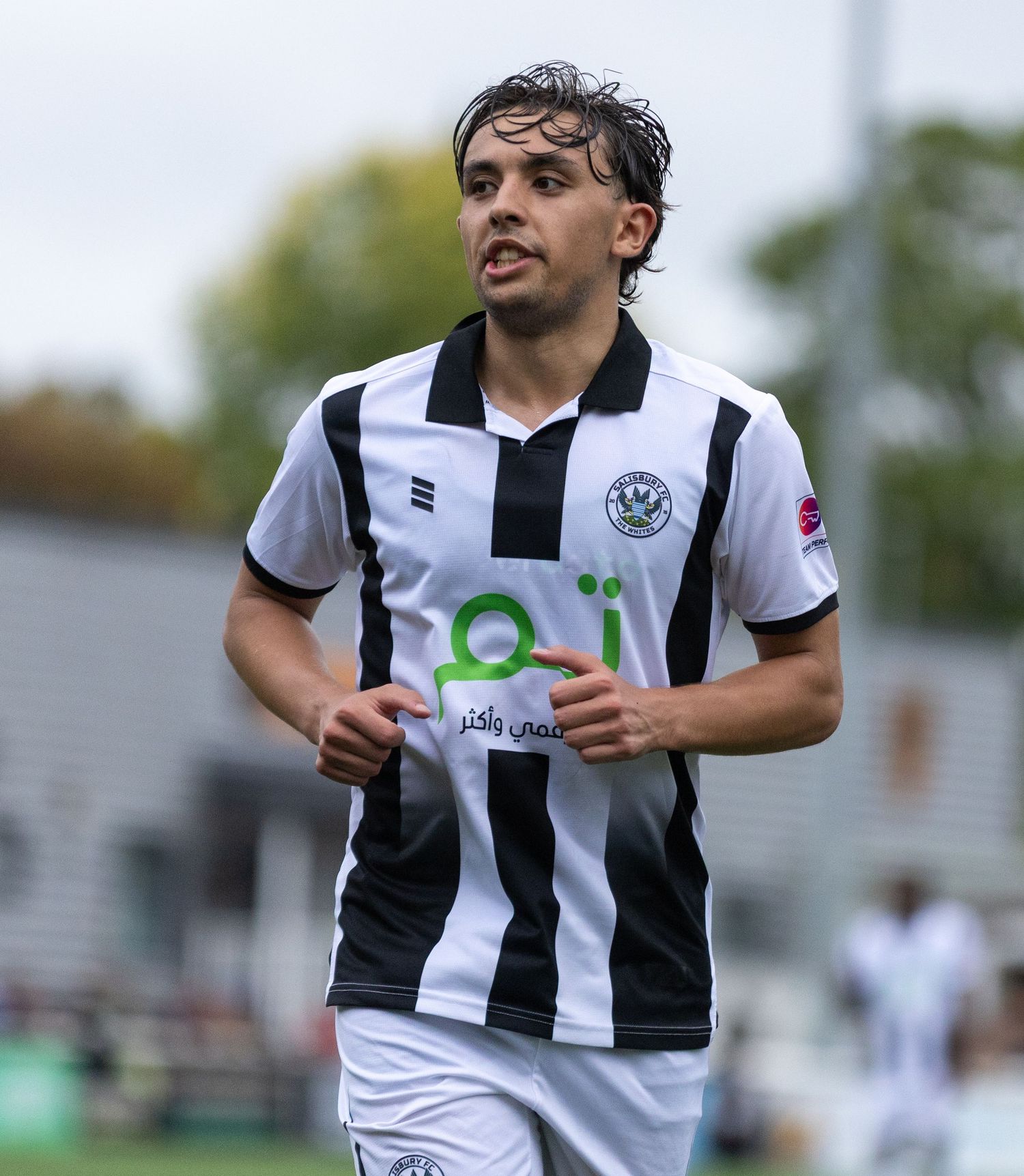 Young male soccer player in black and white striped jersey jogging on field during a match.