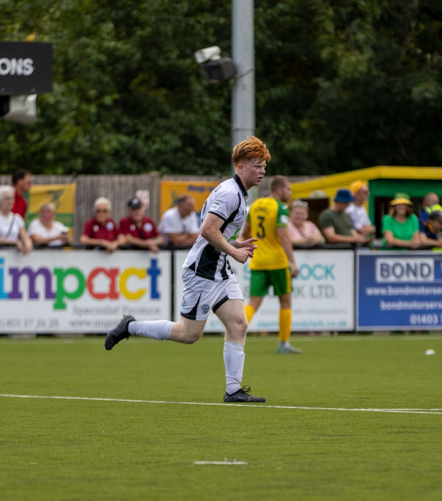 A red-haired footballer in white and black kit sprints across the pitch during a football match.