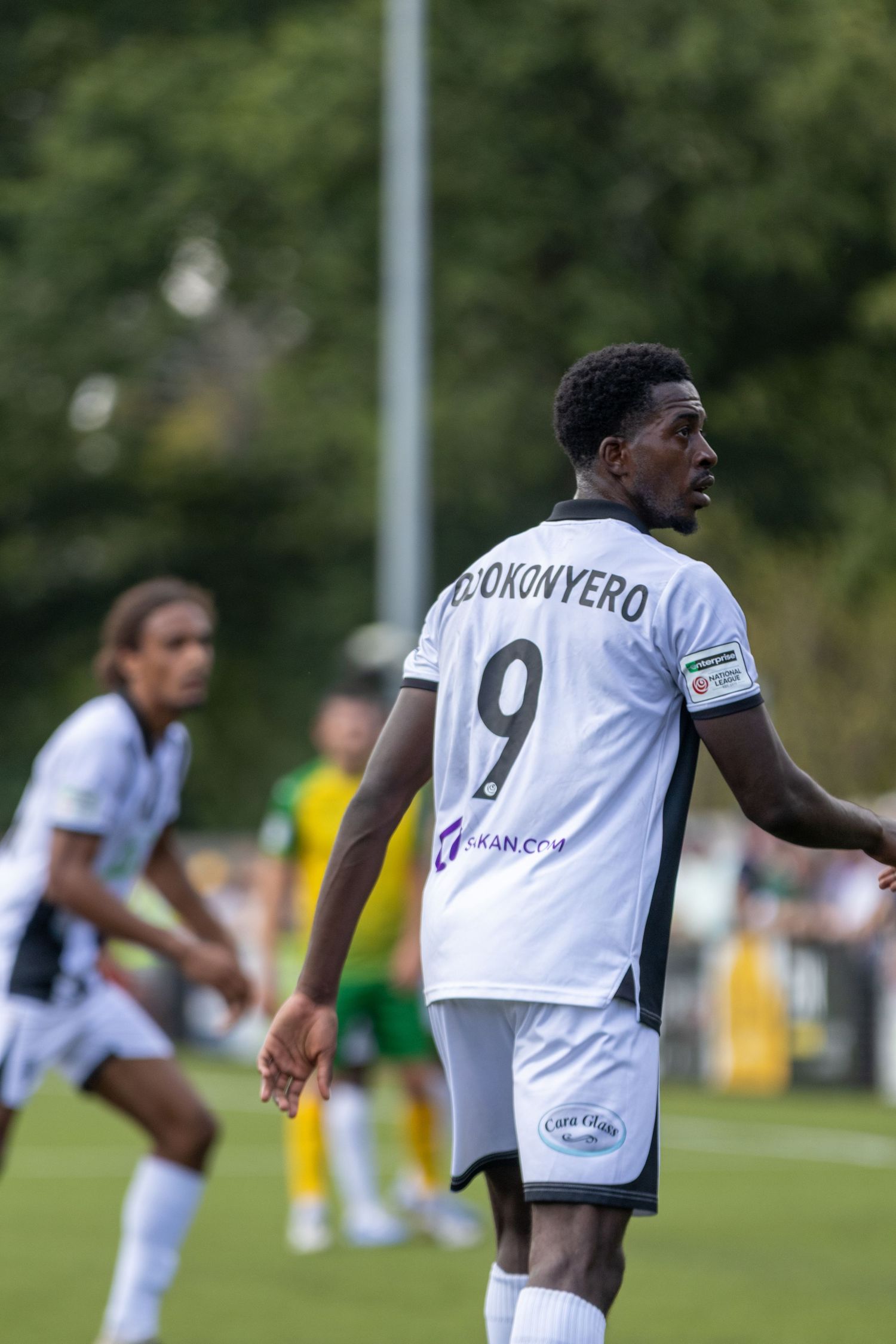Footballer Okonyero wearing number 9 white jersey walks on the pitch during a competitive match.