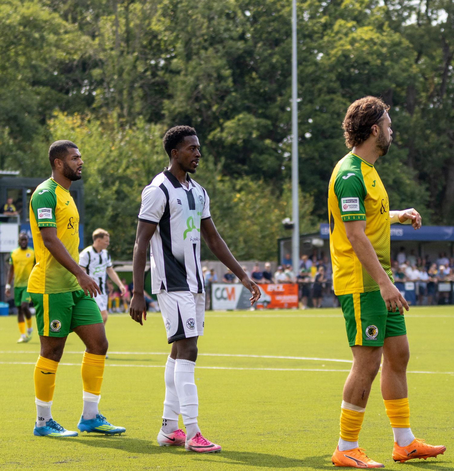 Three football players in white and yellow-green kits stand on the pitch during a match.