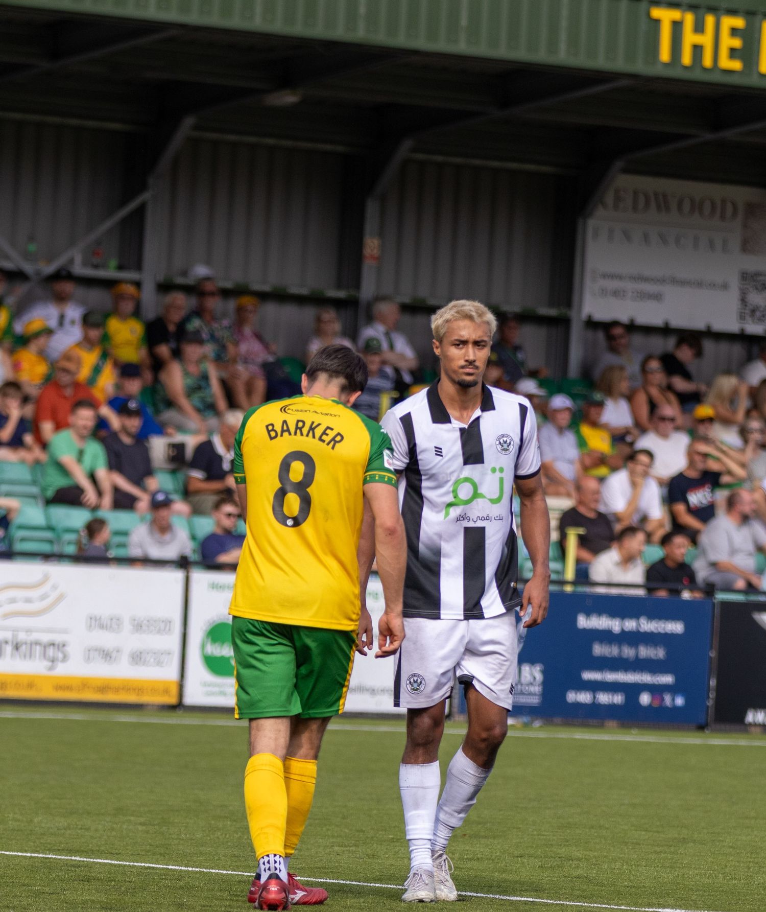 Football players Barker number 8 in yellow and white kit player walk on sunny pitch.
