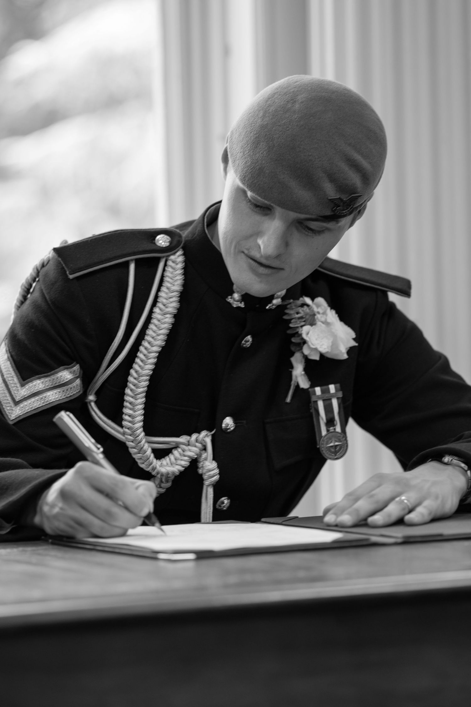 Military groom in dress uniform signs wedding register at wooden desk.