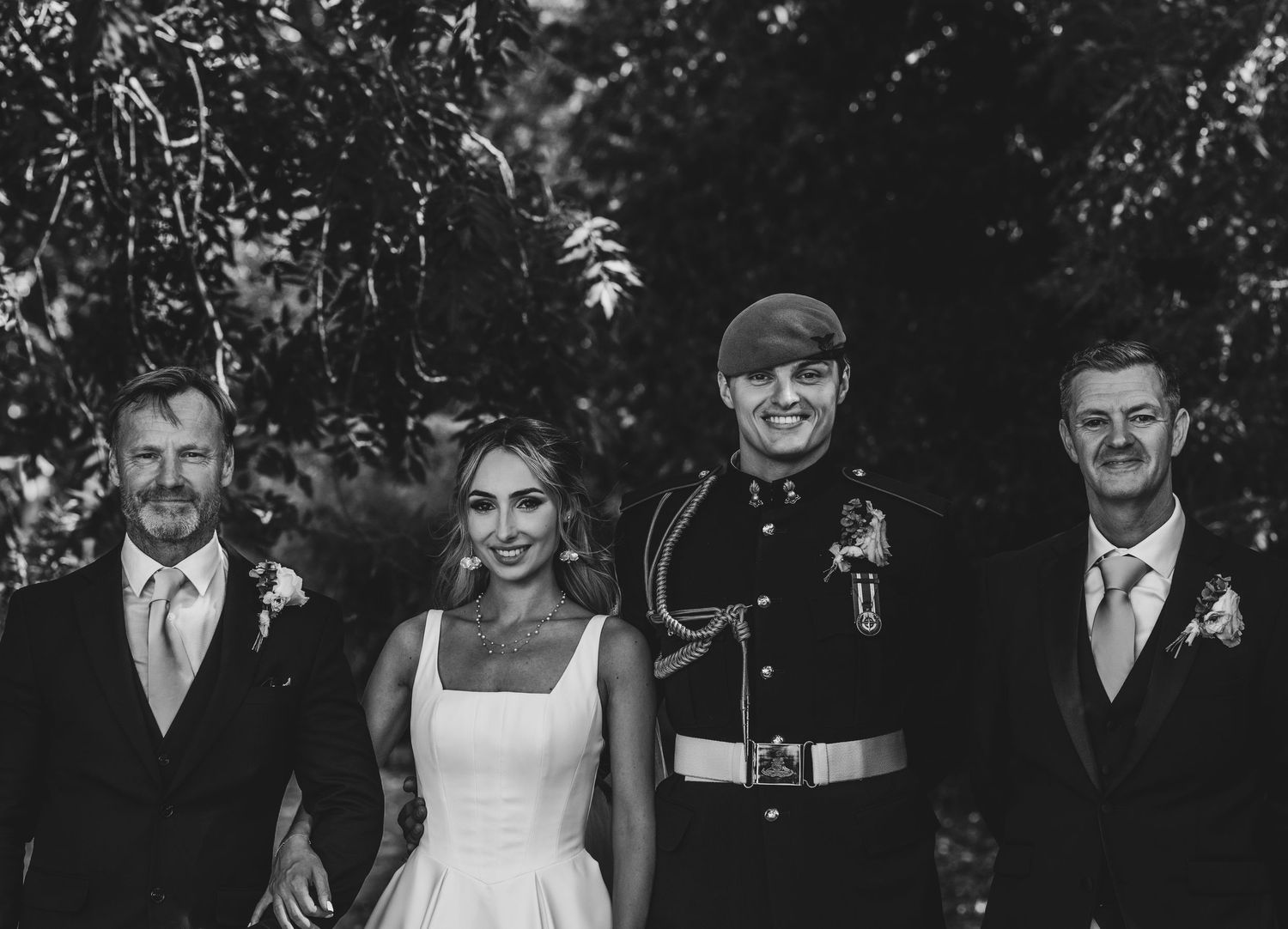 Black and white wedding photo of bride in white gown flanked by three men including one in military uniform.