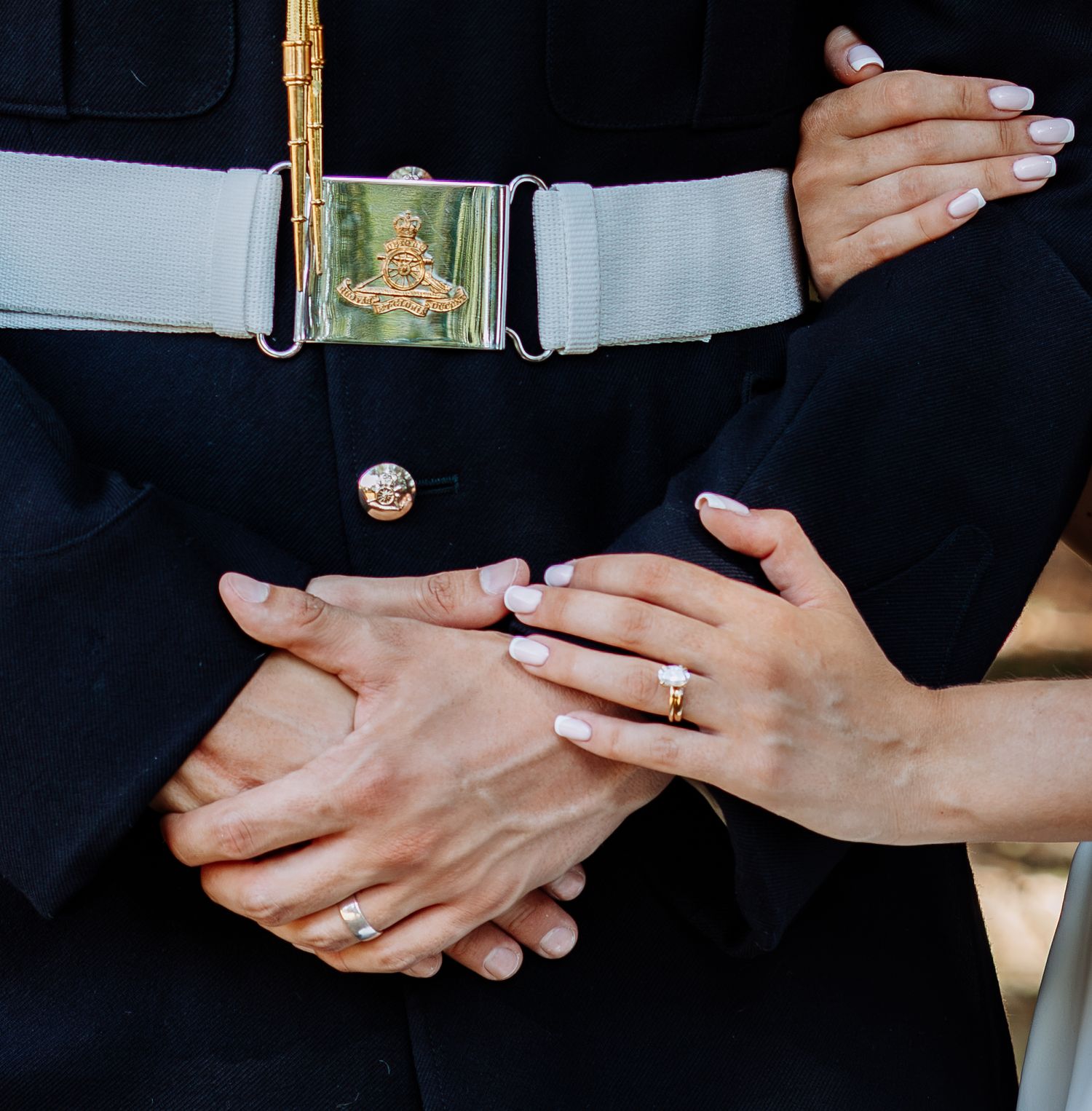 Detail shot of couple's hands with wedding rings, groom wearing military uniform with decorative belt.
