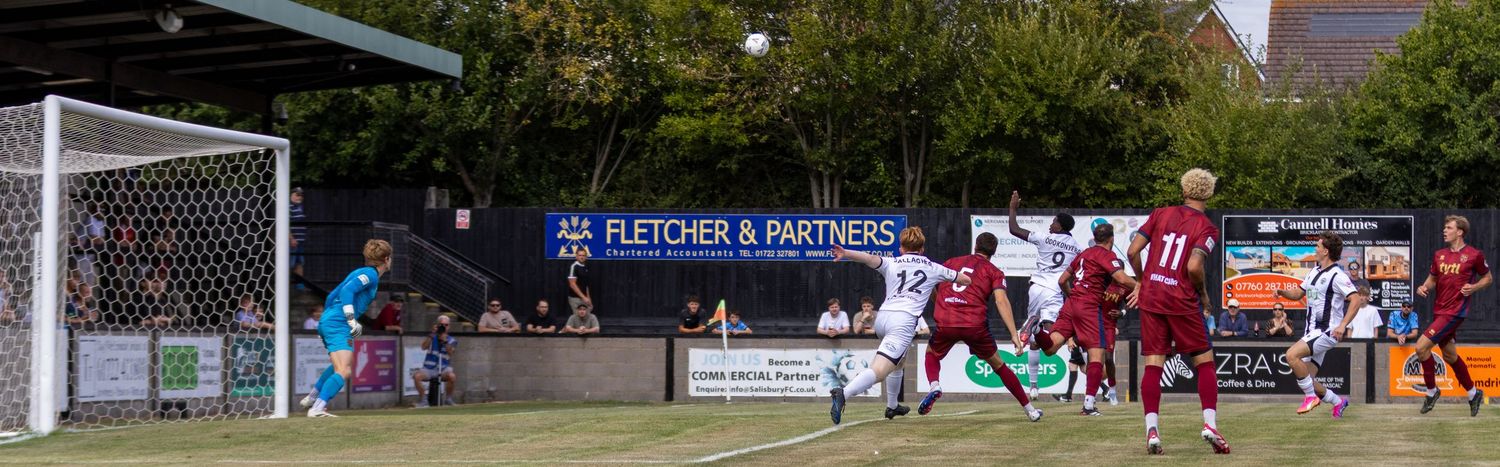 Salisbury FC players challenge for the ball near the goal during an intense football match.