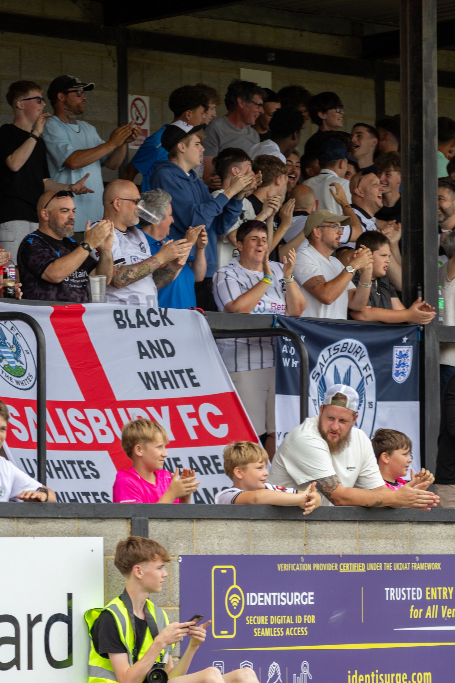 Salisbury FC supporters applauding in the stands with club banner during a home football match.