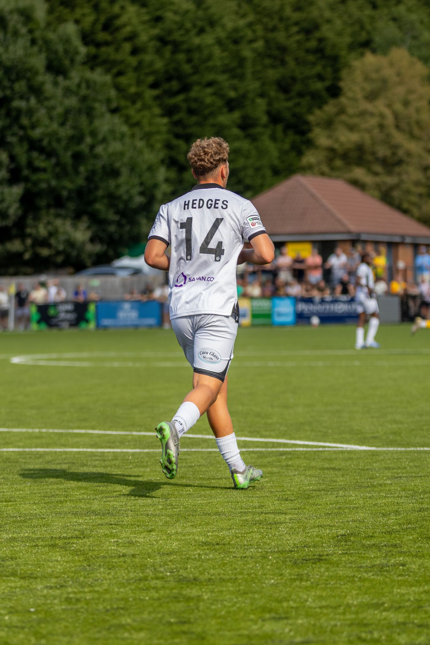 Footballer Hedges number 14 in white away kit strides across the pitch during a sunny outdoor football match.