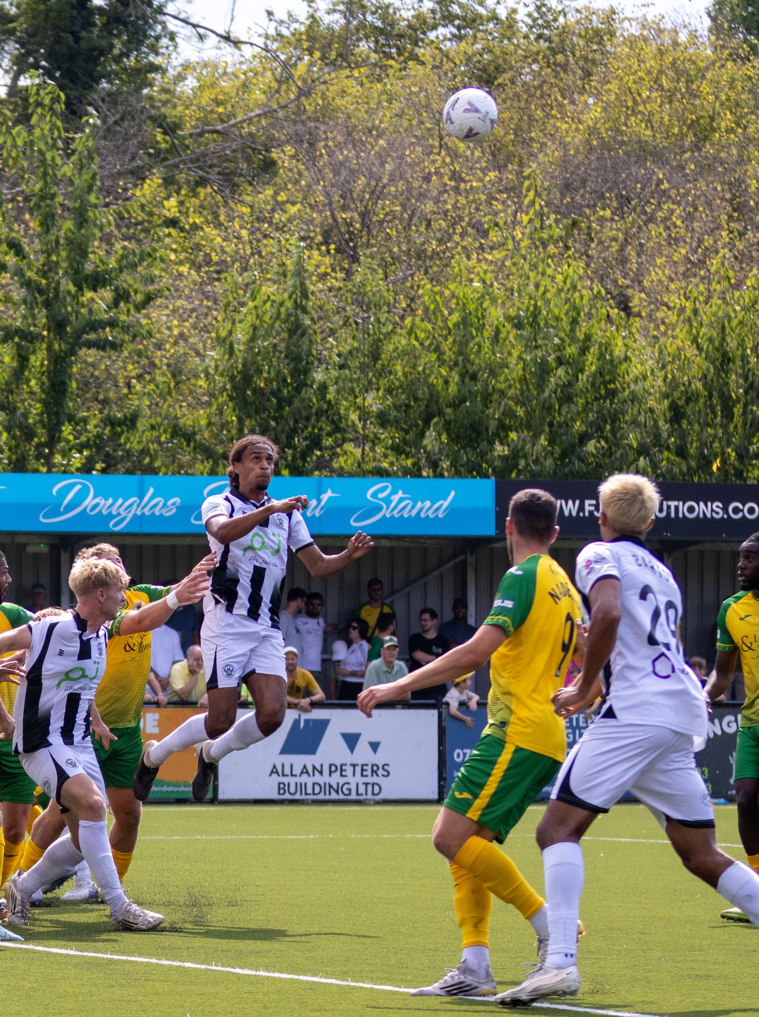 Footballer in black and white kit heads the ball during a competitive match outdoors.