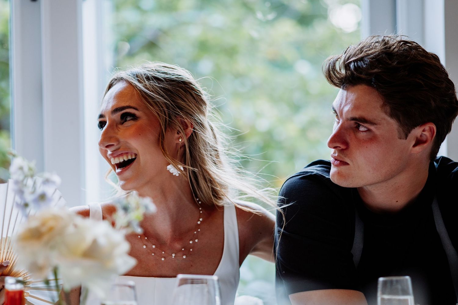Bride and groom smiling at wedding reception table with champagne glasses and flowers.