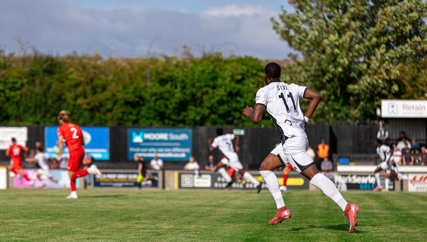 Soccer player wearing number 11 jersey sprints on a sunny outdoor pitch during a competitive football match.