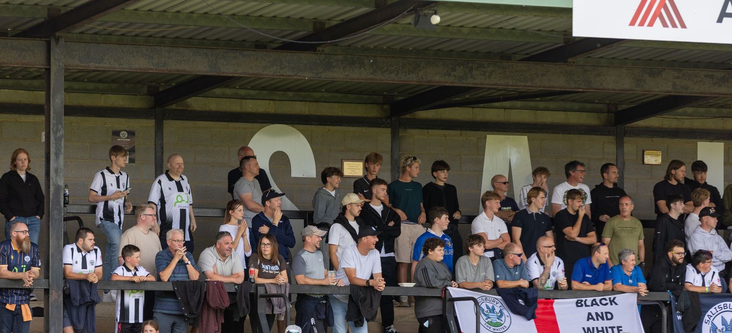 Crowd of spectators watching a match from a covered stand at a football ground.