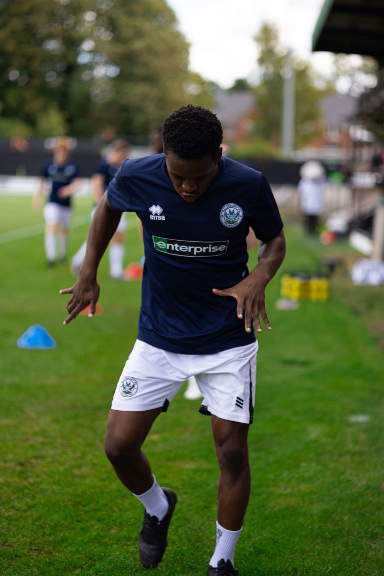 A young soccer player in a navy Enterprise-sponsored jersey and white shorts practices agility drills on a green grass field.