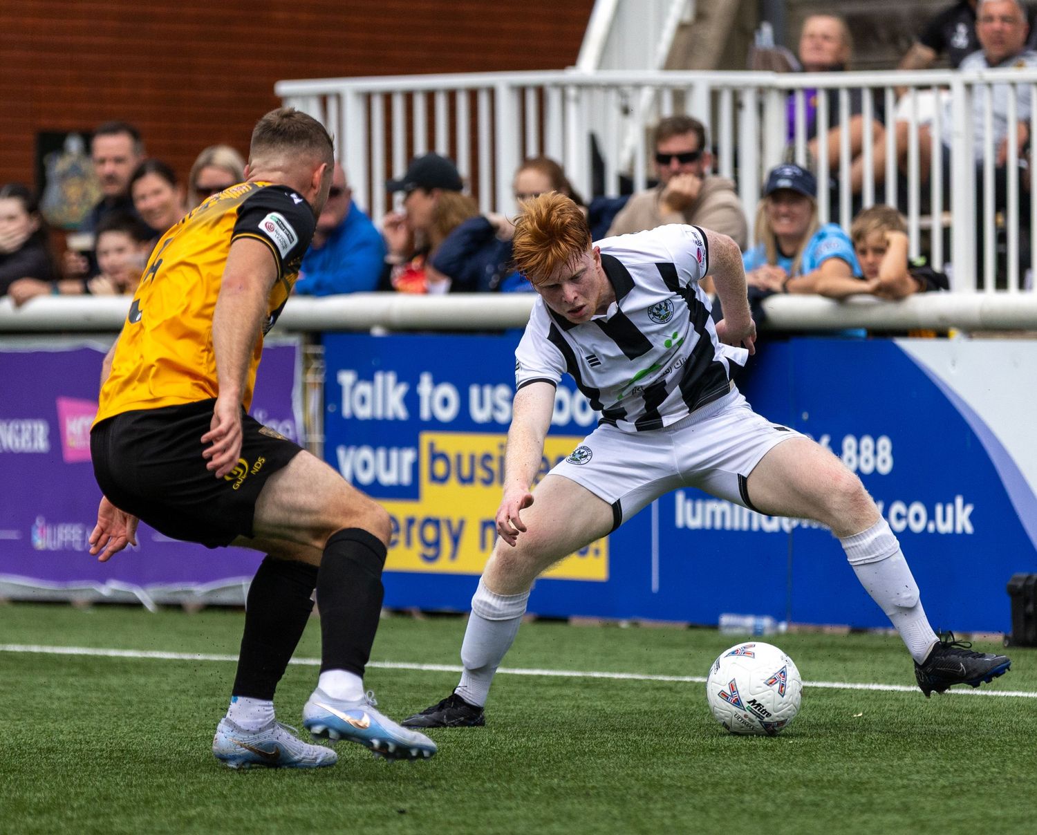 Two soccer players compete for the ball during a match, one in black and white stripes, the other in yellow and black.