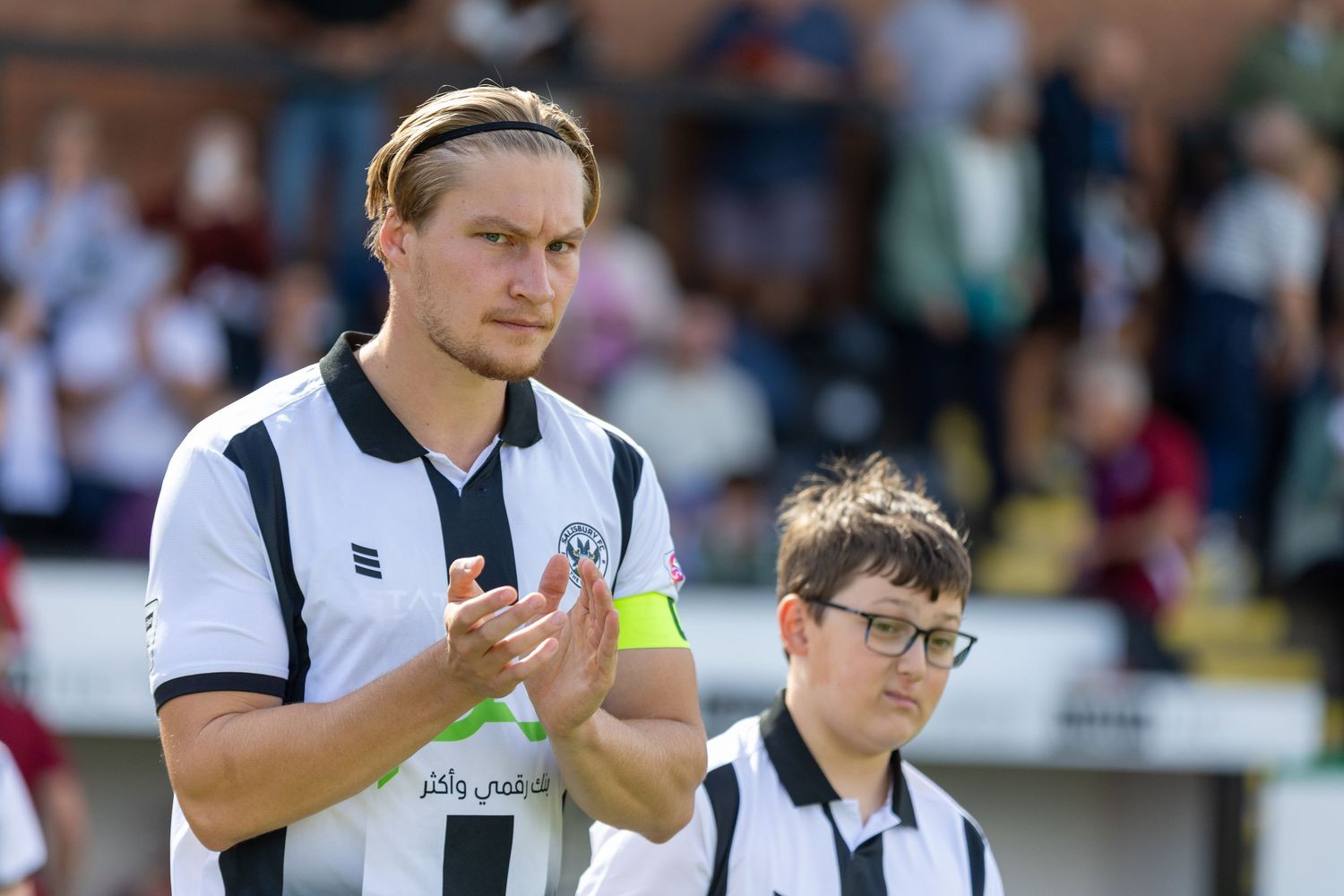 Two soccer players in black and white striped jerseys applauding fans on the field during a match.