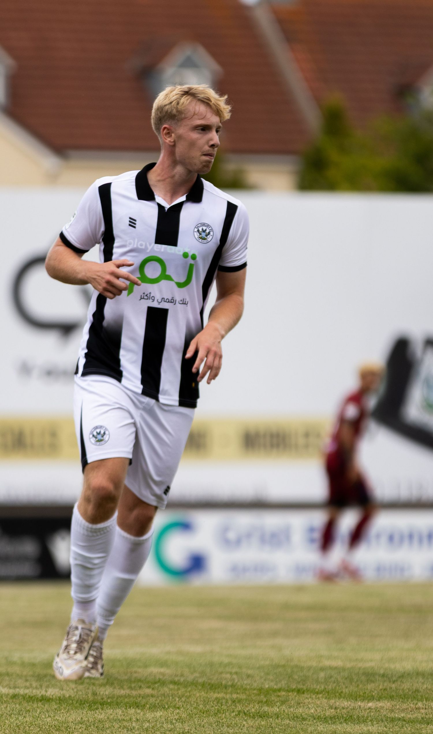 A blonde footballer in black and white striped kit with AJ sponsor runs during a match.