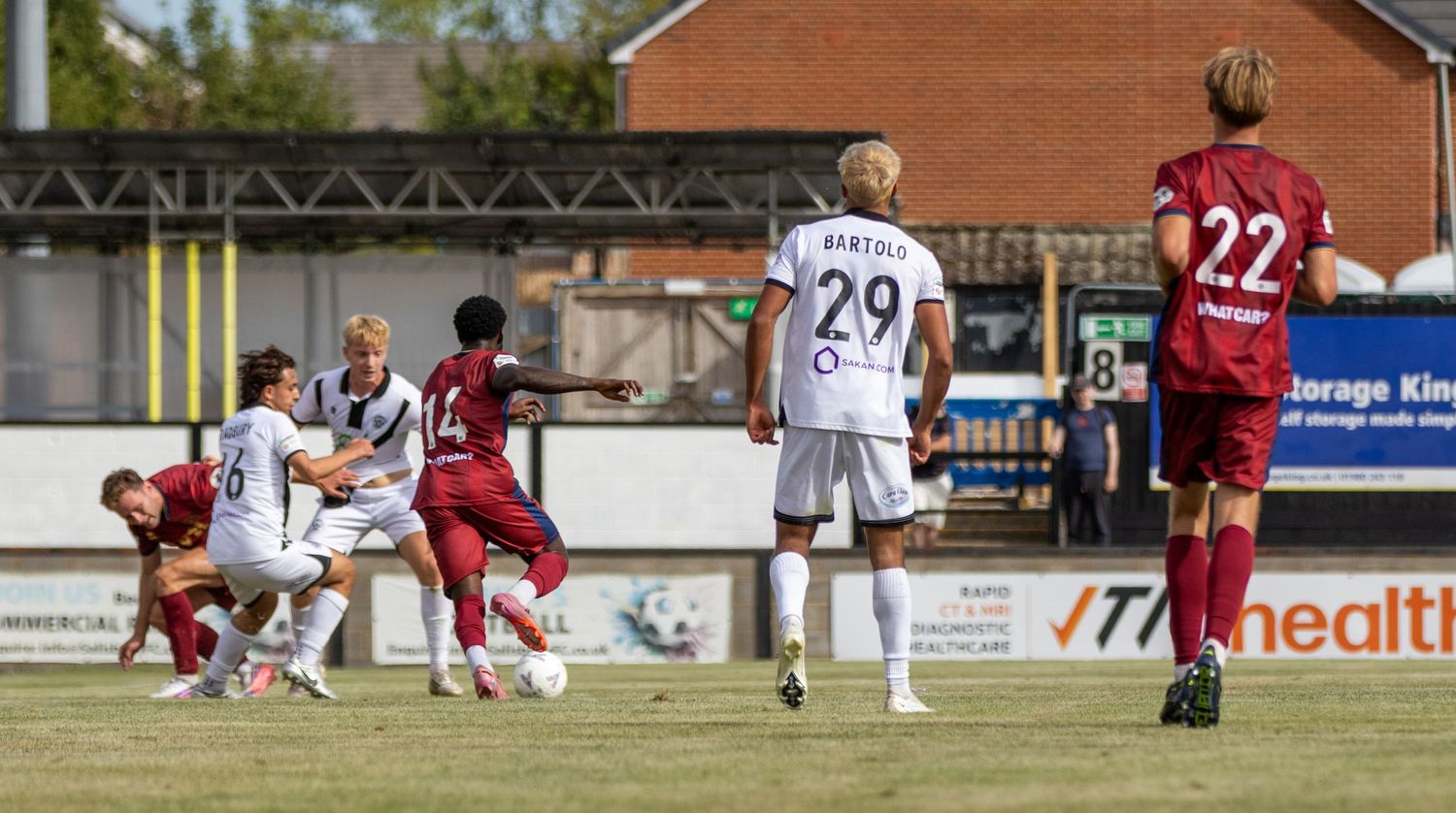 Non-league football players contest a set piece with player 29 visible during a sunny match.