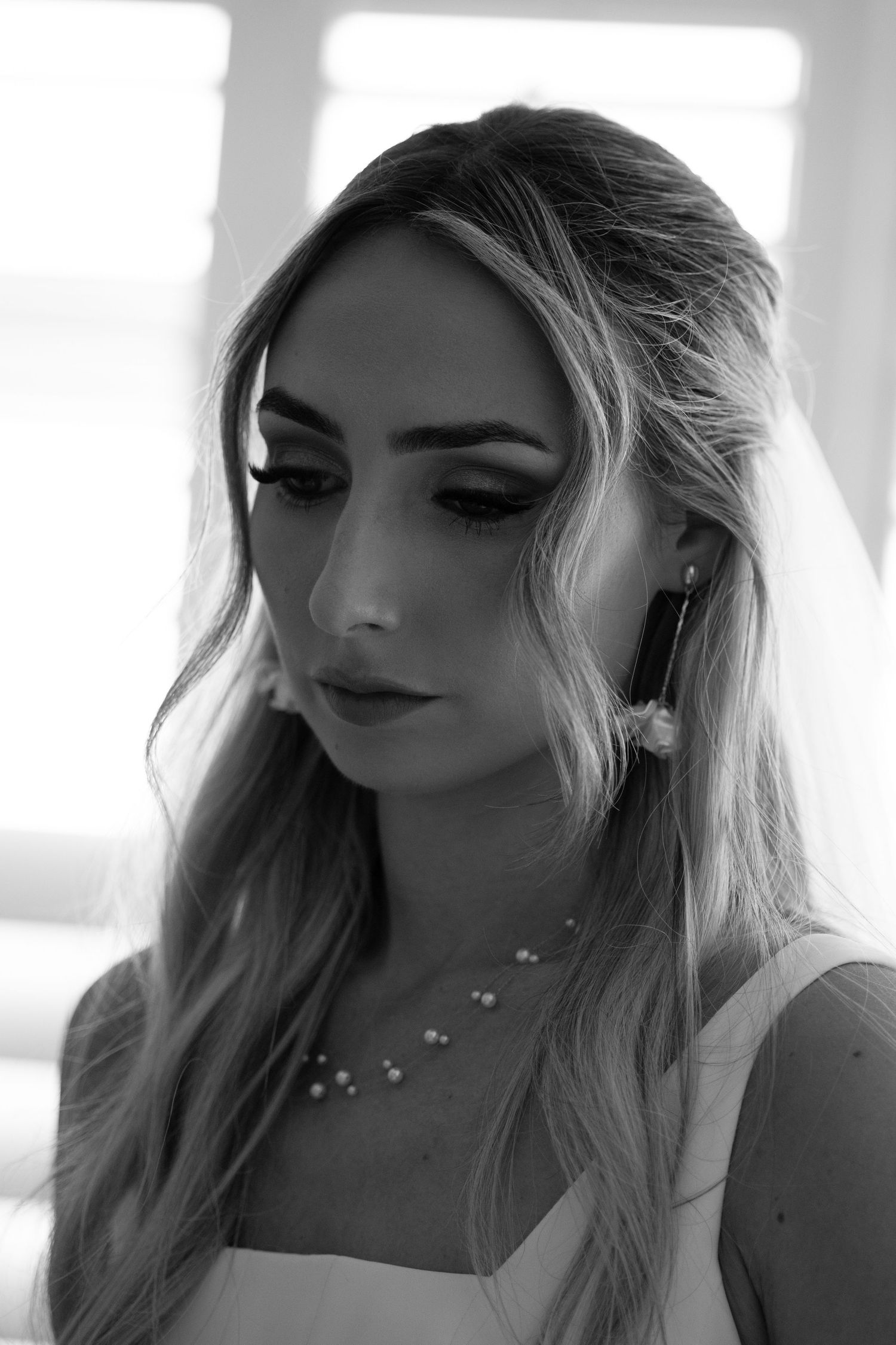 Black and white bridal portrait of woman with wavy hair wearing pearl necklace and drop earrings.