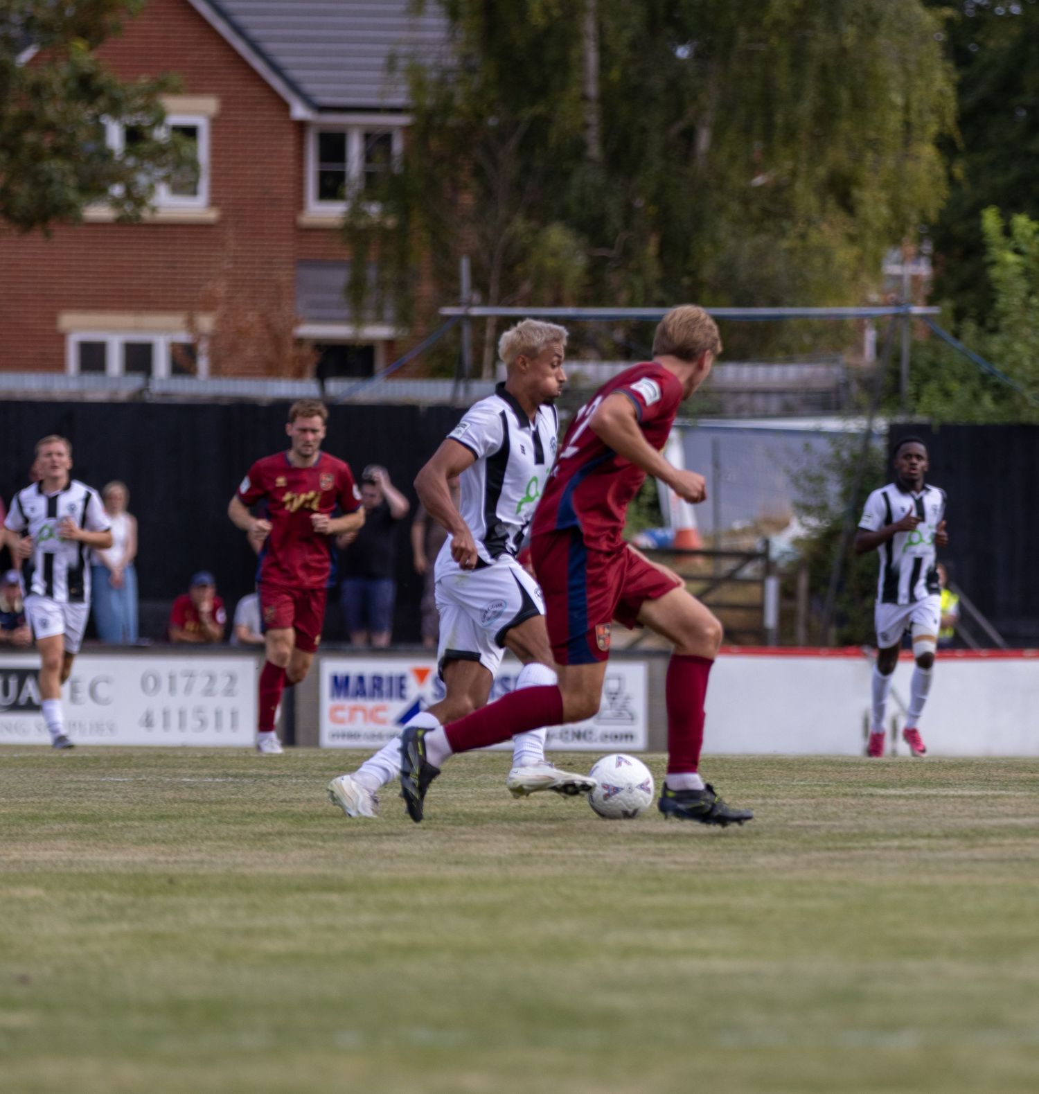 Two football players battle for possession during a match on a grass pitch with spectators in background.